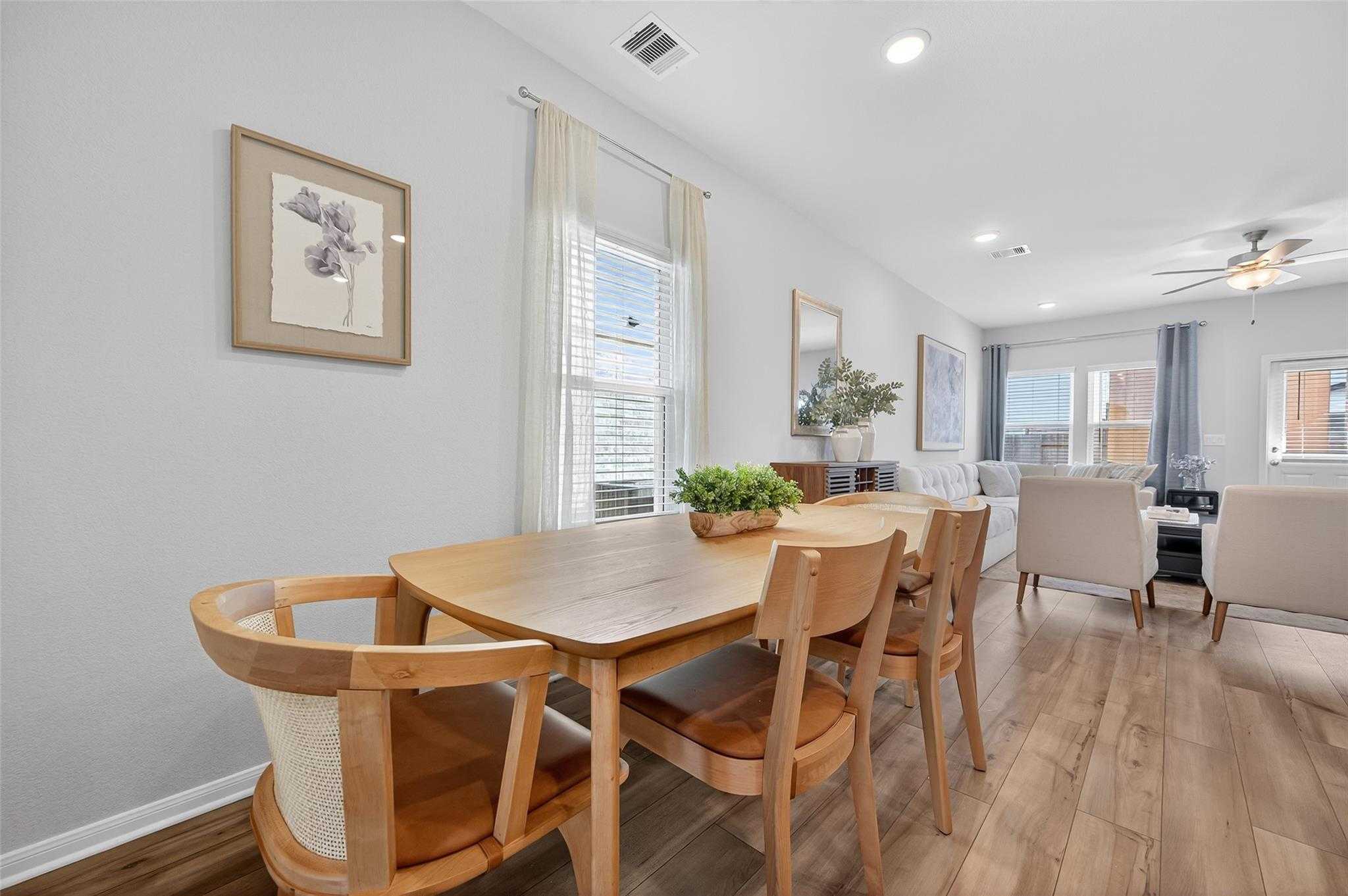 Modern dining room with oak table, rattan chairs, potted plants, and sheer curtains in The Brazos E by Davidson Homes, Magnolia, Texas