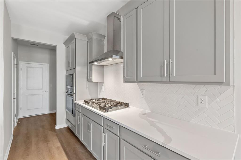 Modern kitchen with gray shaker cabinets, white quartz counters, stainless gas range and herringbone backsplash in The Marion A, Winder GA