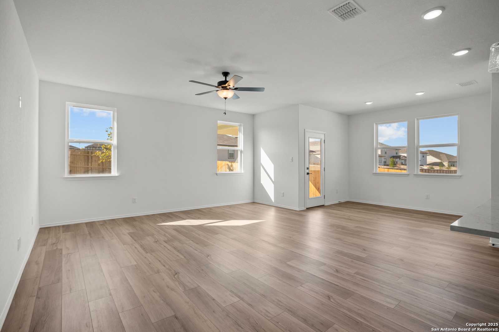 Bright open living room with hardwood floors, ceiling fan, large windows, and sliding door in Davidson Homes The Daphne K, San Antonio