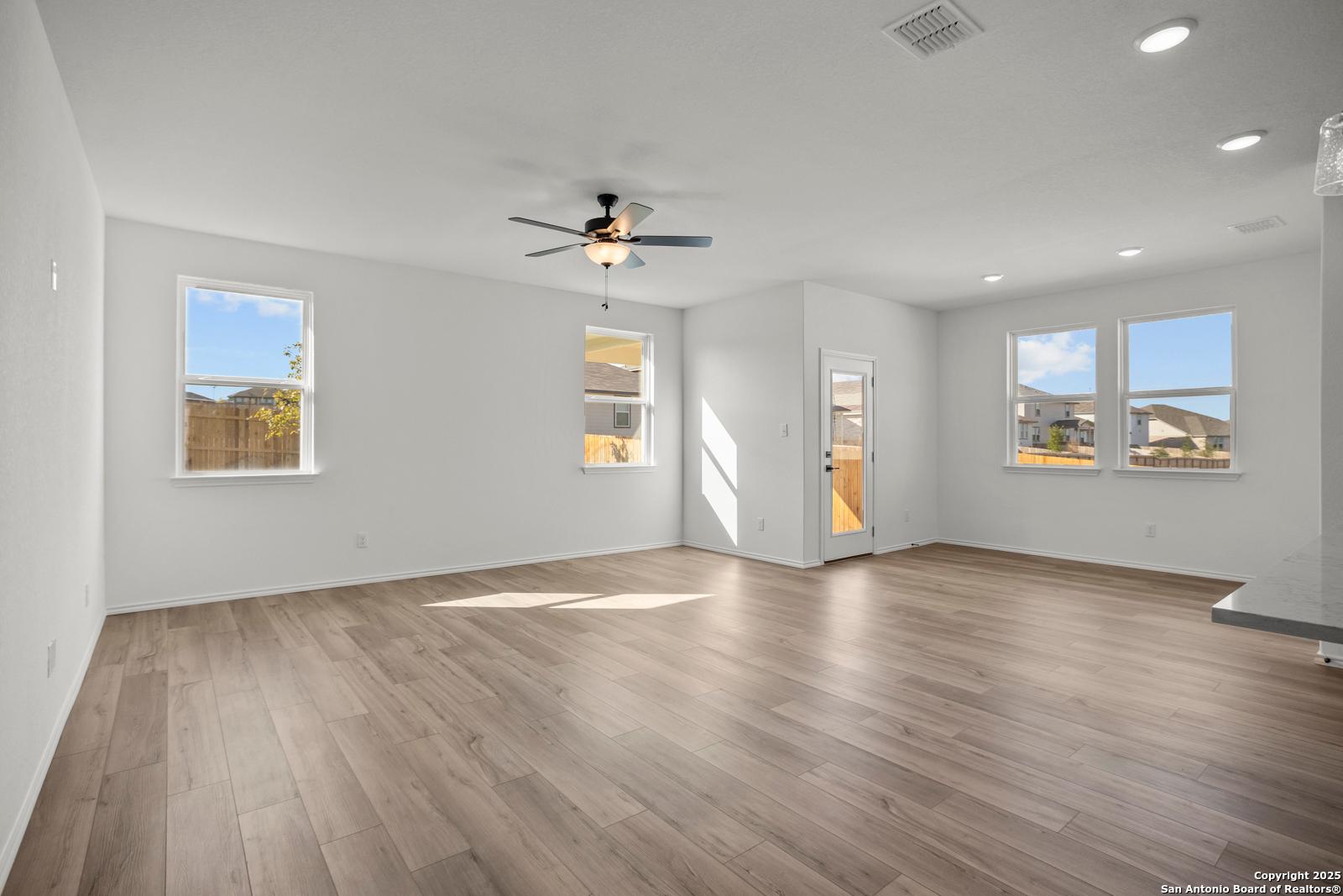 Bright open living room with hardwood floors, ceiling fan, large windows, and sliding door in Davidson Homes The Daphne K, San Antonio