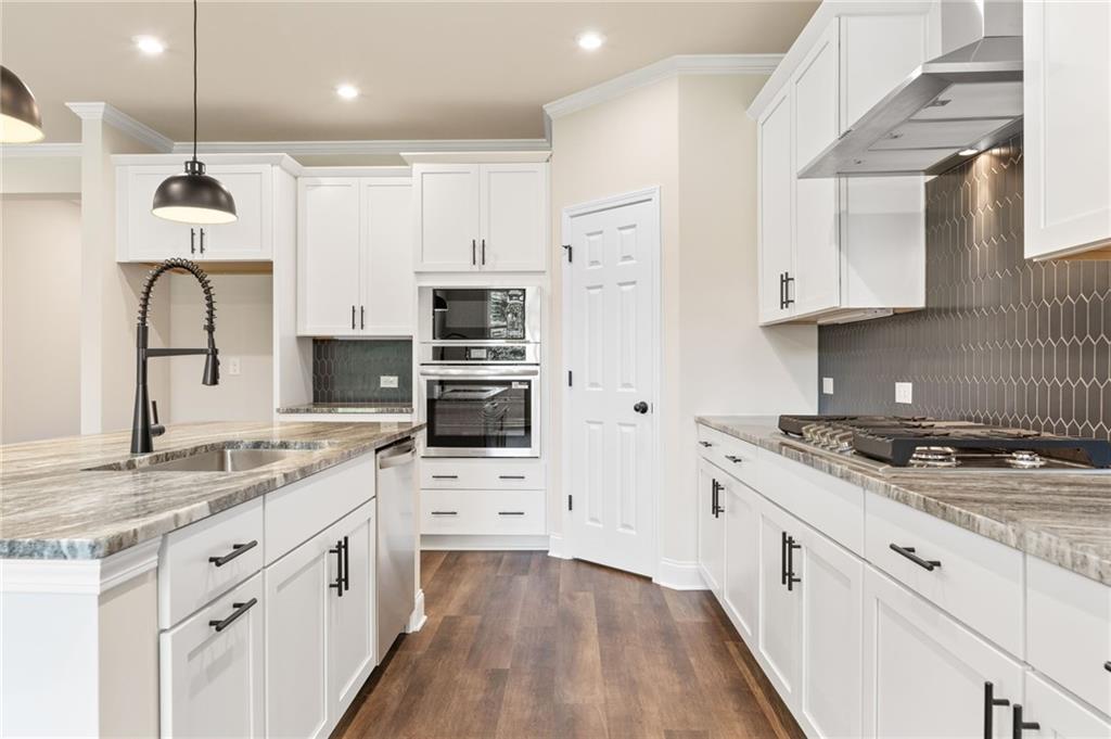 Modern white shaker kitchen with granite island, pull-out faucet, stainless double oven, hex metallic backsplash in The Harrison H, Winder, GA
