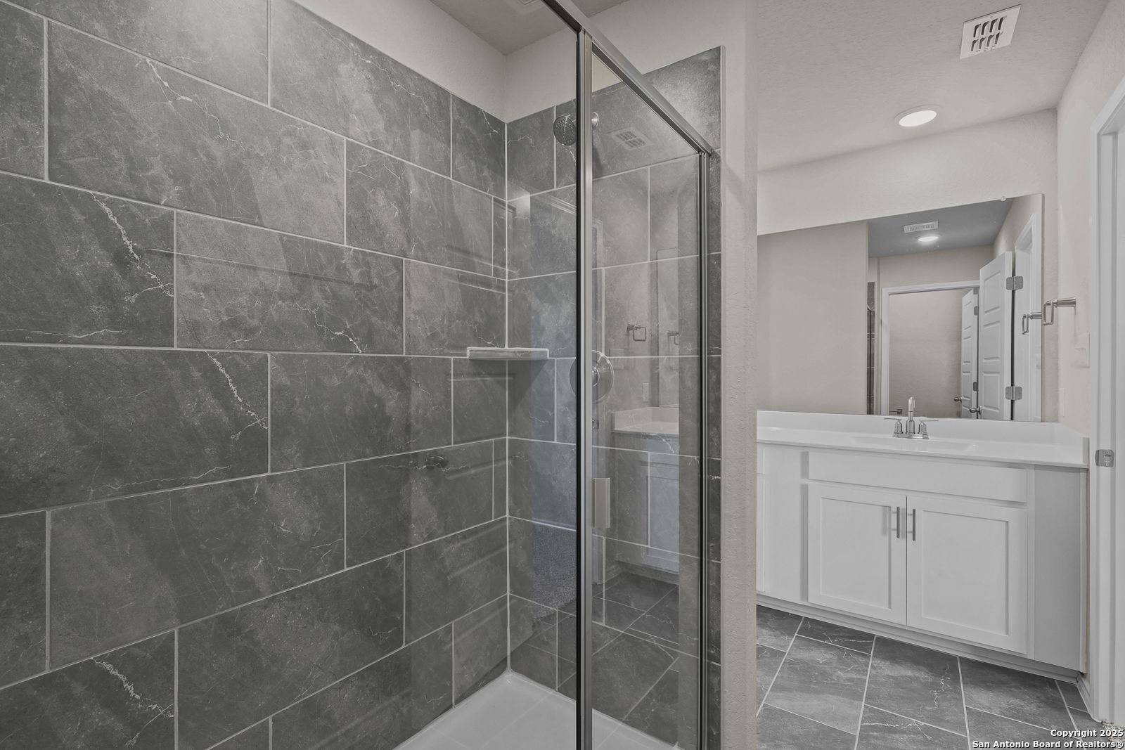 Modern master bathroom featuring gray tile shower enclosure and double vanity in Davidson Homes The Trinity D, San Antonio