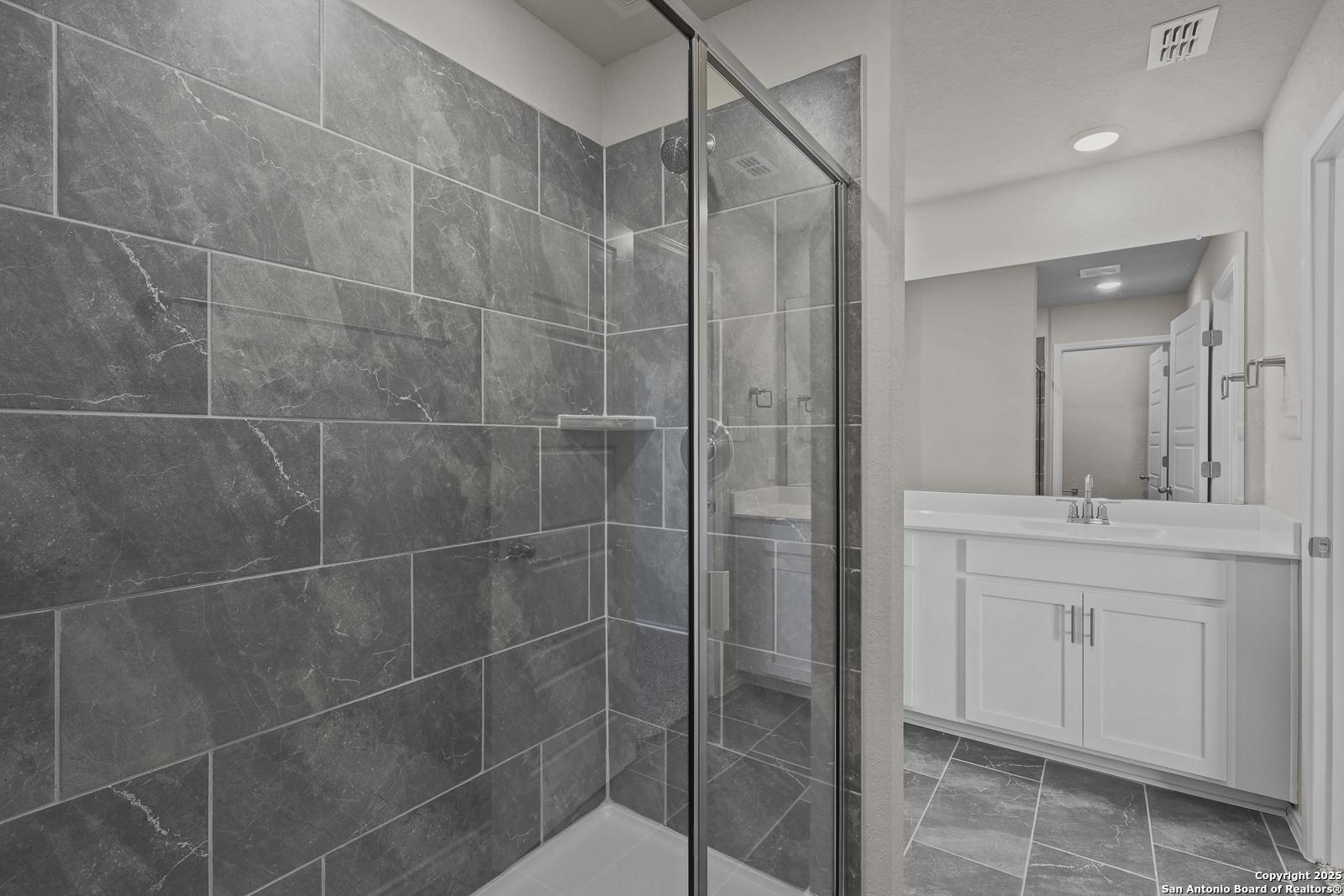 Modern master bathroom featuring gray tile shower enclosure and double vanity in Davidson Homes The Trinity D, San Antonio