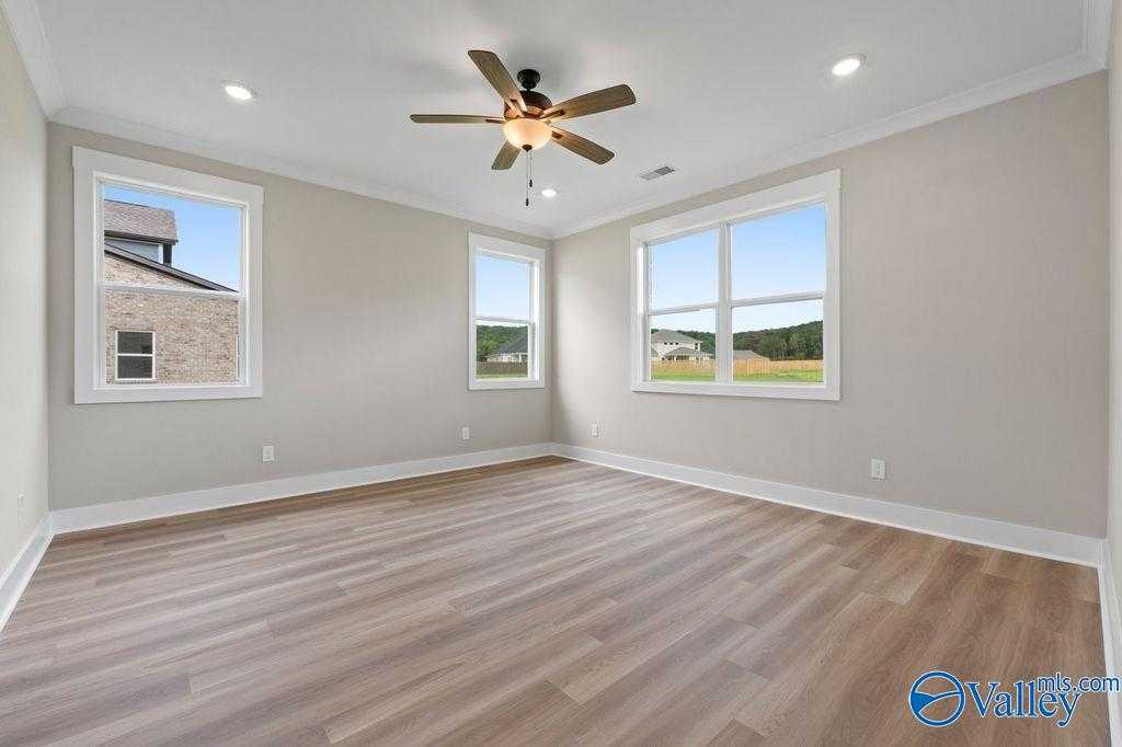 Bright bedroom with hardwood floors, ceiling fan, and large windows overlooking neighborhood in Evermore Homes The Oxford, Owens Cross Roads, Alabama