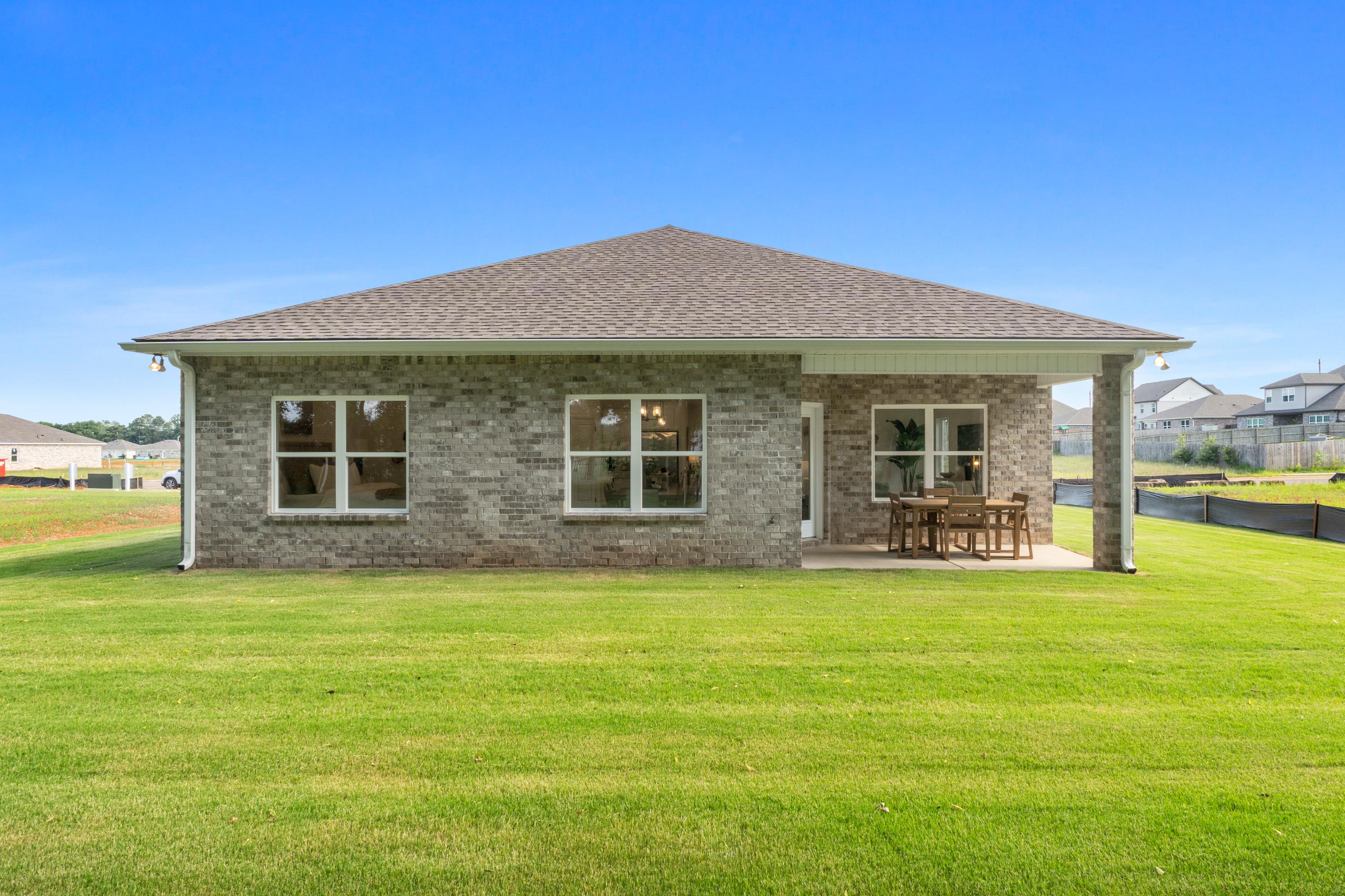 Brick home rear exterior at Lynn Meadows in Meridianville Alabama with covered patio, outdoor seating and pond view