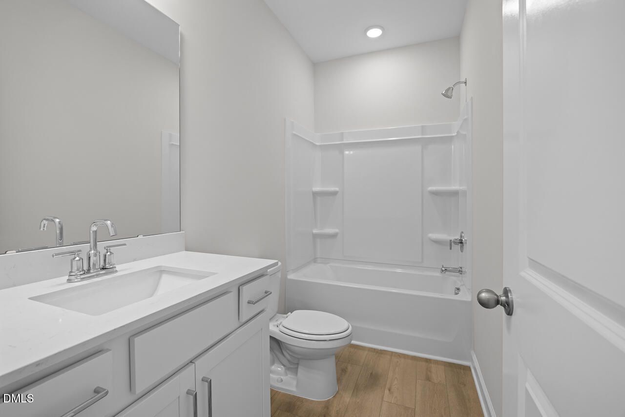 Bright white bathroom with vanity, tub-shower combo, and wood-look flooring in Davidson Homes The Daphne D, Zebulon, NC