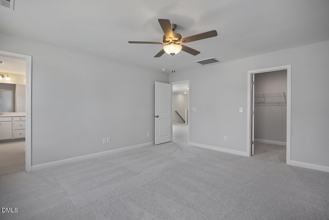 Spacious bedroom with carpet, ceiling fan, and walk-in closet in The Adalynn B floor plan at Gregory Village, Lillington, NC.