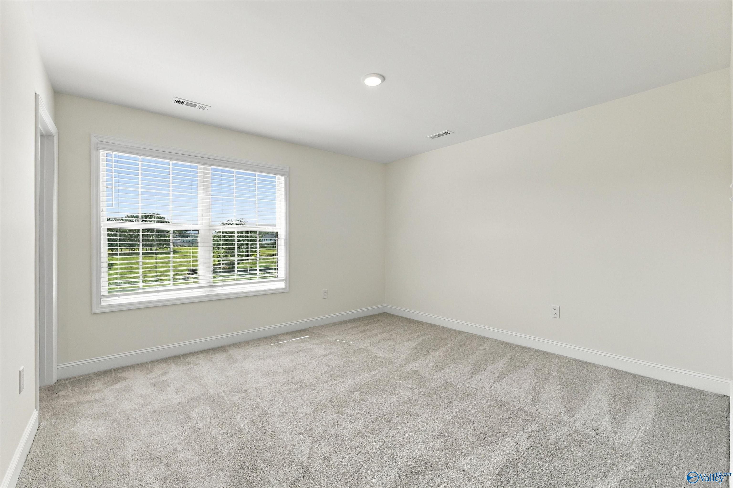 Bright empty bedroom with plush carpet and white shutters overlooking green views in Davidson Homes Valencia plan, Huntsville