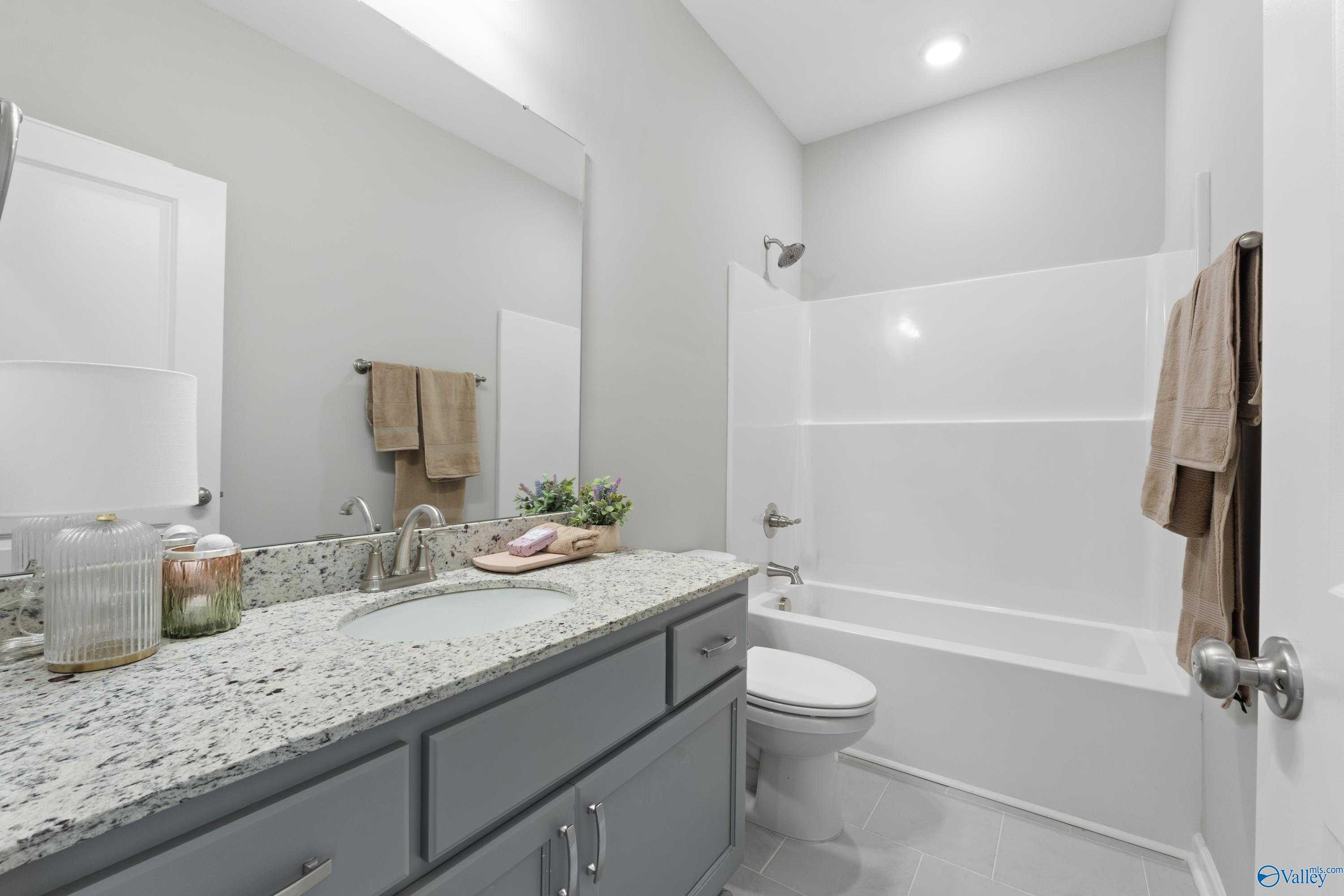 Modern bathroom with granite vanity, gray cabinets, tub-shower combo in Davidson Homes The Luna, Hazel Green, Alabama