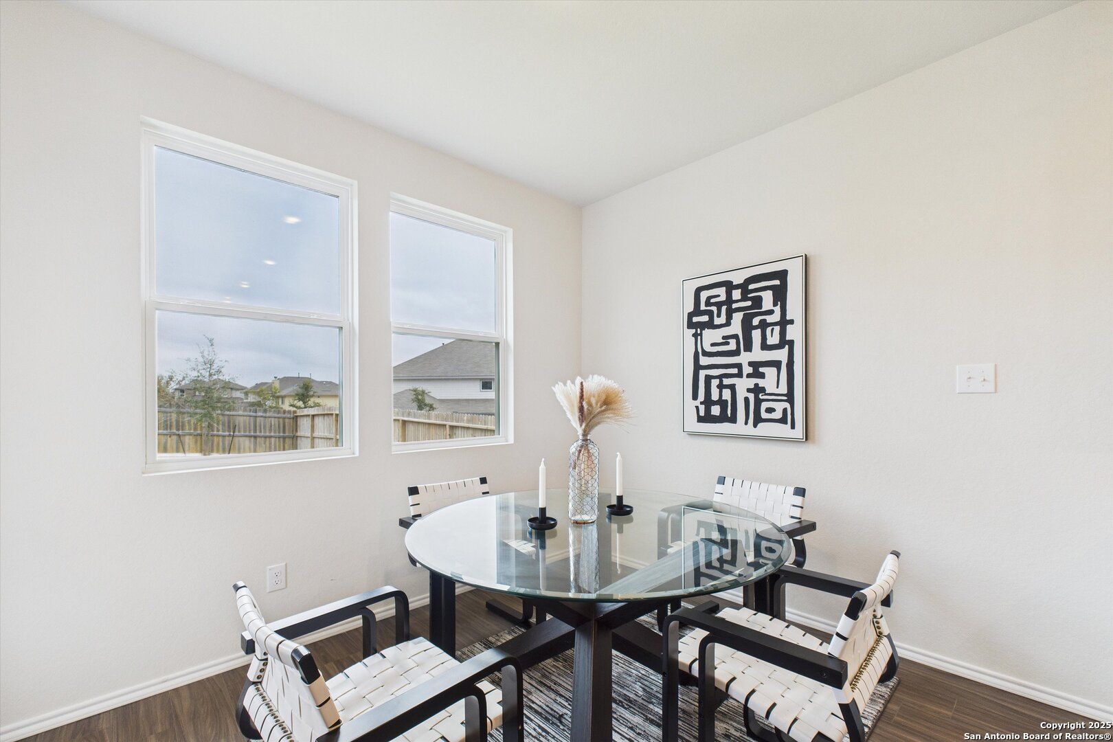 Modern dining nook with round glass table, rattan chairs, vase centerpiece, and large windows in The Asheville K home, Bricewood, San Antonio