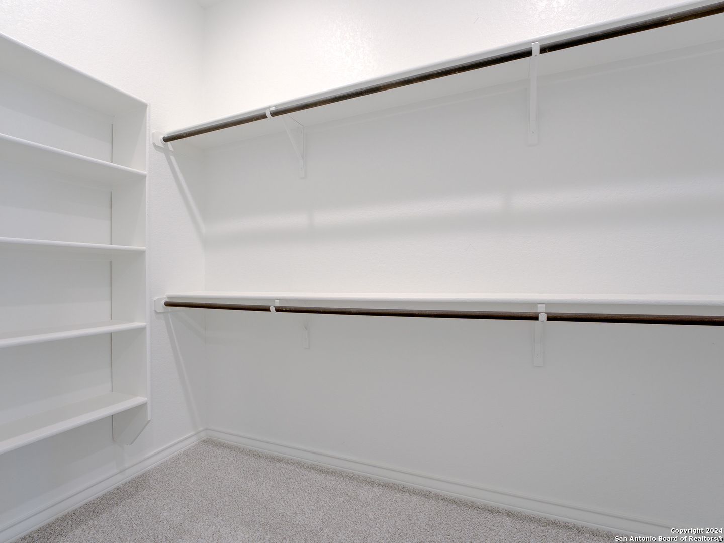 Spacious walk-in closet with white built-in shelves and hanging rods in Davidson Homes The Summerlin A, Castroville, Texas