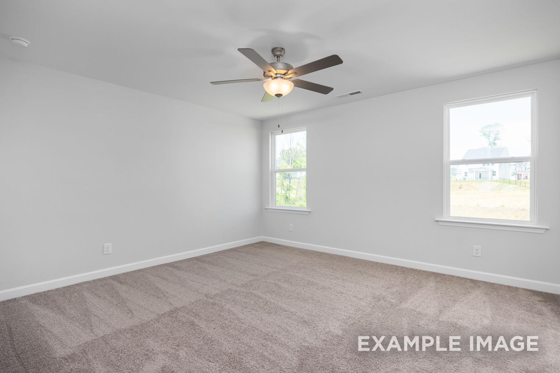Spacious empty master bedroom in The Gavin B with neutral gray walls, beige carpet, ceiling fan, and large windows for natural light