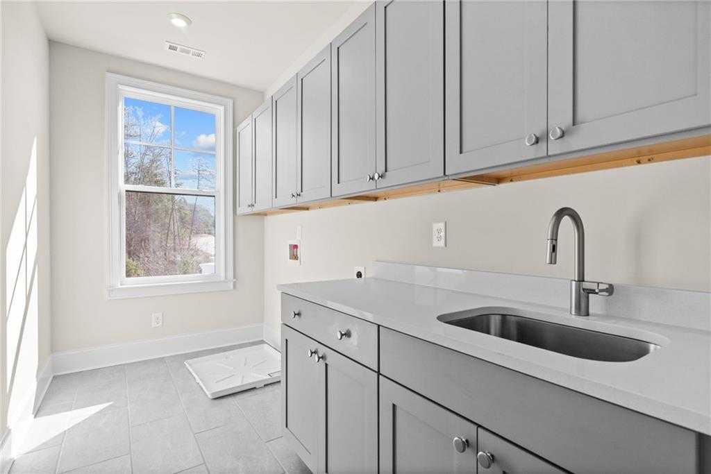 Bright laundry room with gray shaker cabinets, quartz countertop, utility sink, and window view in Davidson Homes The Arlington A, East Cobb