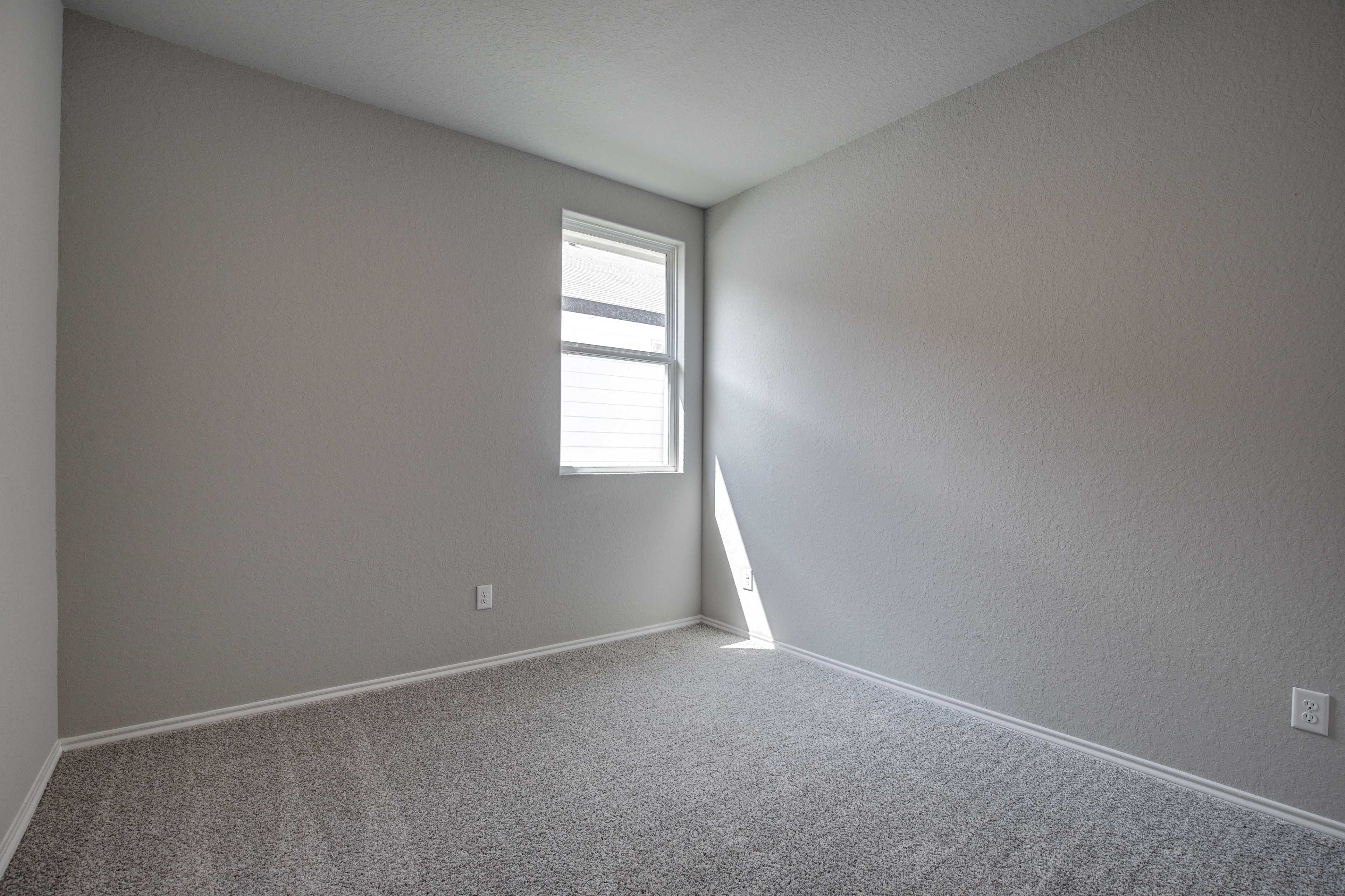 Spacious secondary bedroom in The Asheville home with neutral gray walls, beige carpet, and sunlit window with blinds