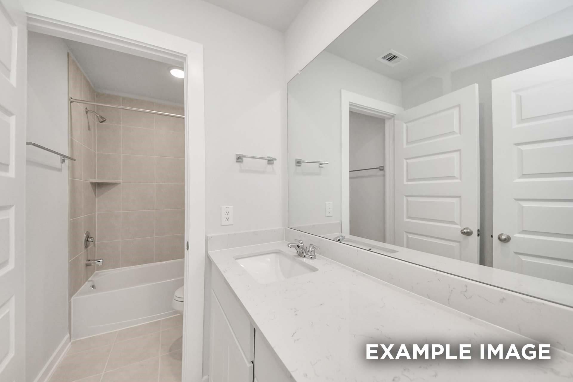 Bright bathroom with quartz countertop, tiled tub shower, and large mirror in Davidson Homes The Blanco E, Magnolia, Texas