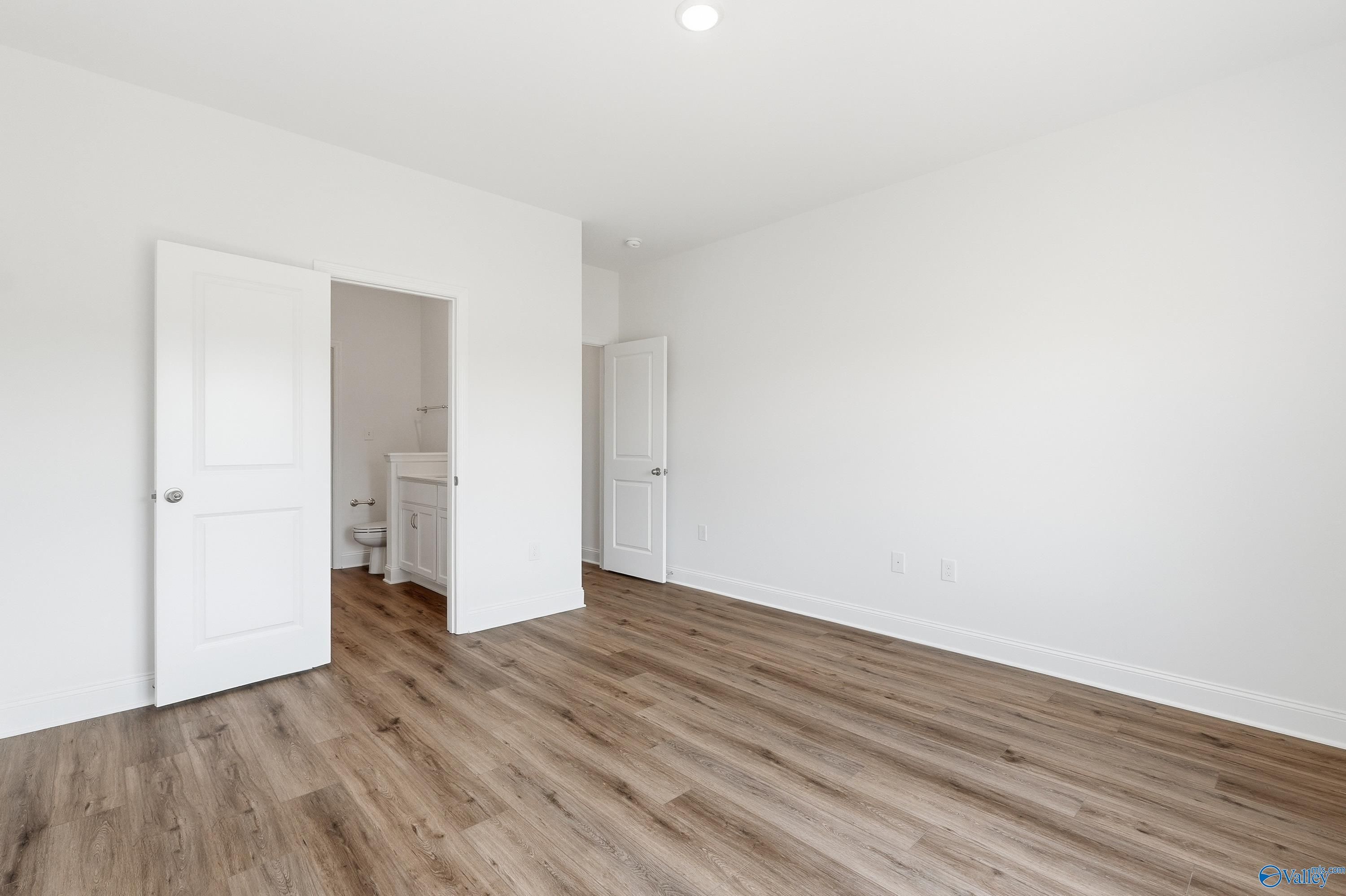 Bright bedroom with wood-look flooring and en-suite bathroom in The Asheville floor plan at Jaguar Hills, Huntsville.