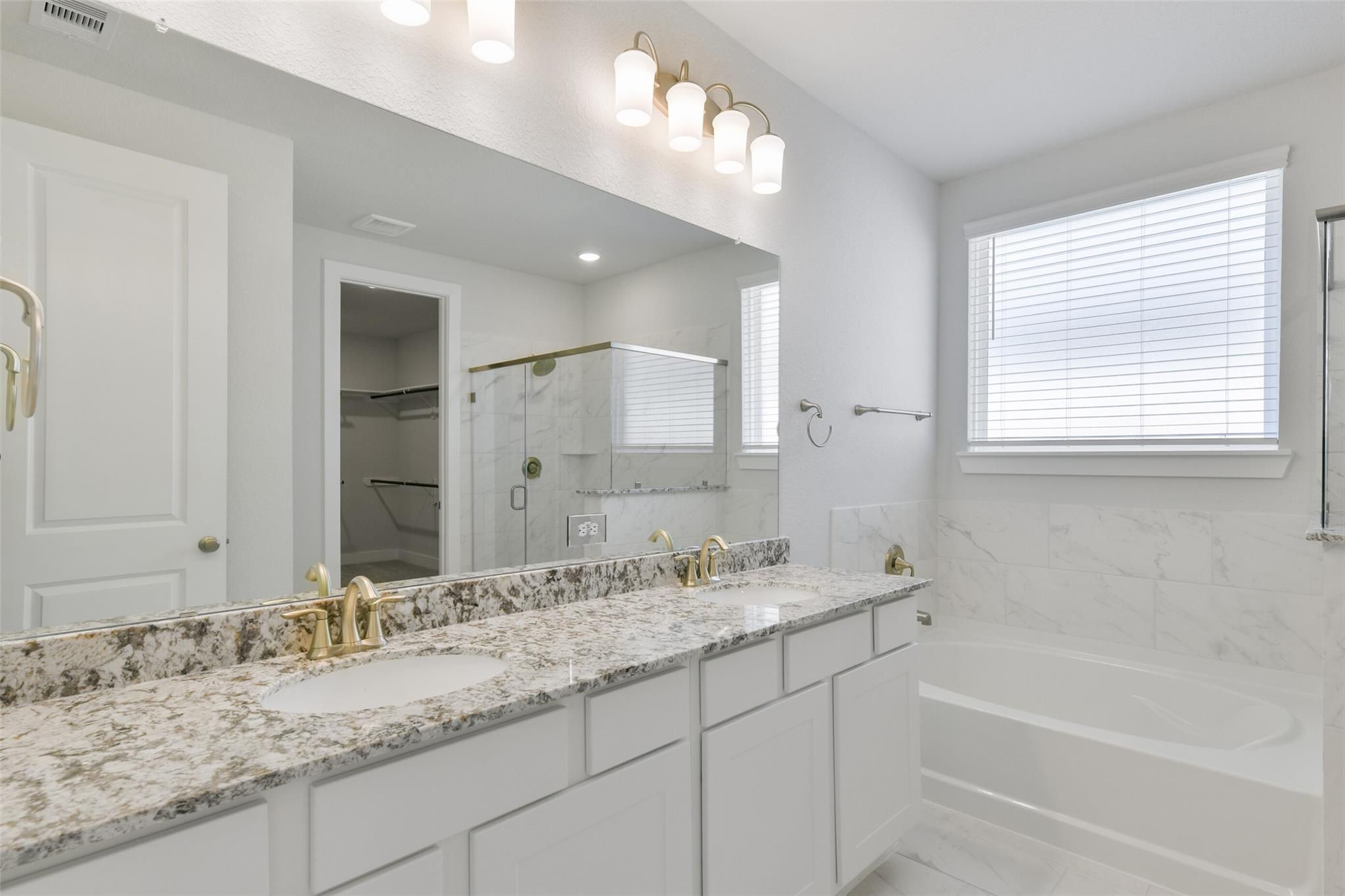 Elegant master bathroom with double quartz vanity, gold fixtures, soaking tub, and glass shower in Davidson Homes The Edward A, Lago Mar