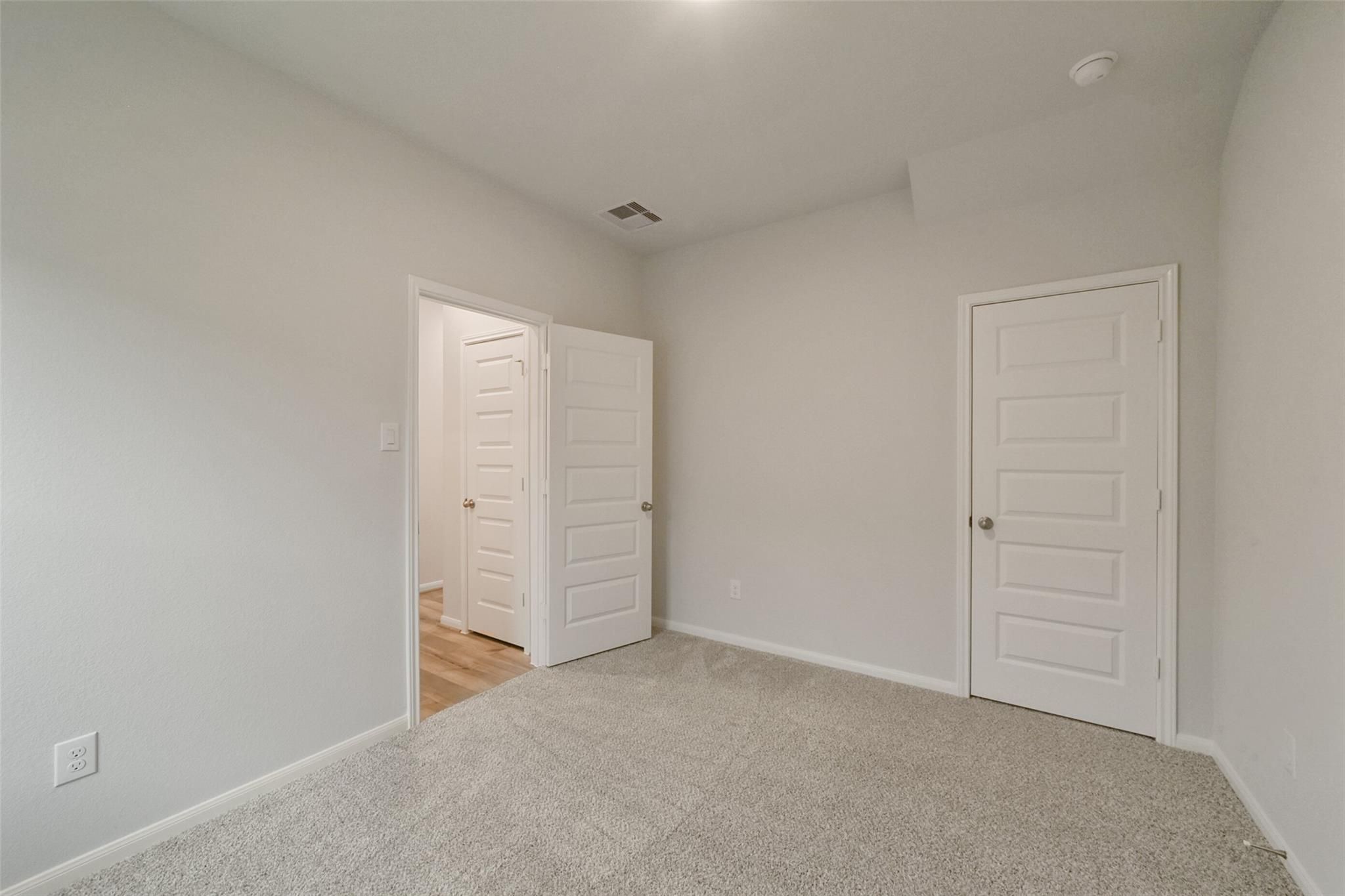 Empty secondary bedroom with light gray walls, neutral carpet, and white paneled doors in Davidson Homes The San Marcos E, Beasley Texas