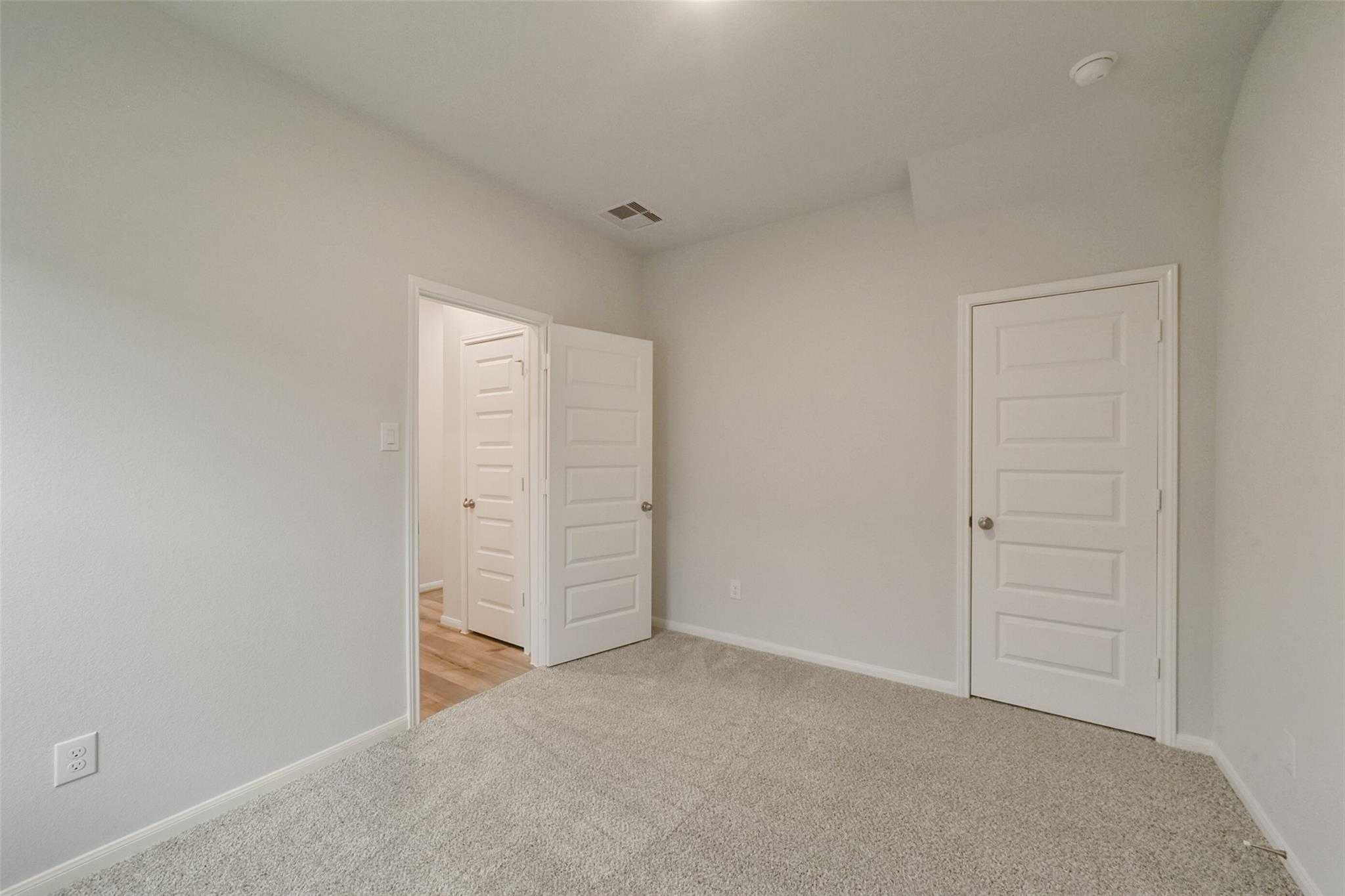 Empty secondary bedroom with light gray walls, neutral carpet, and white paneled doors in Davidson Homes The San Marcos E, Beasley Texas