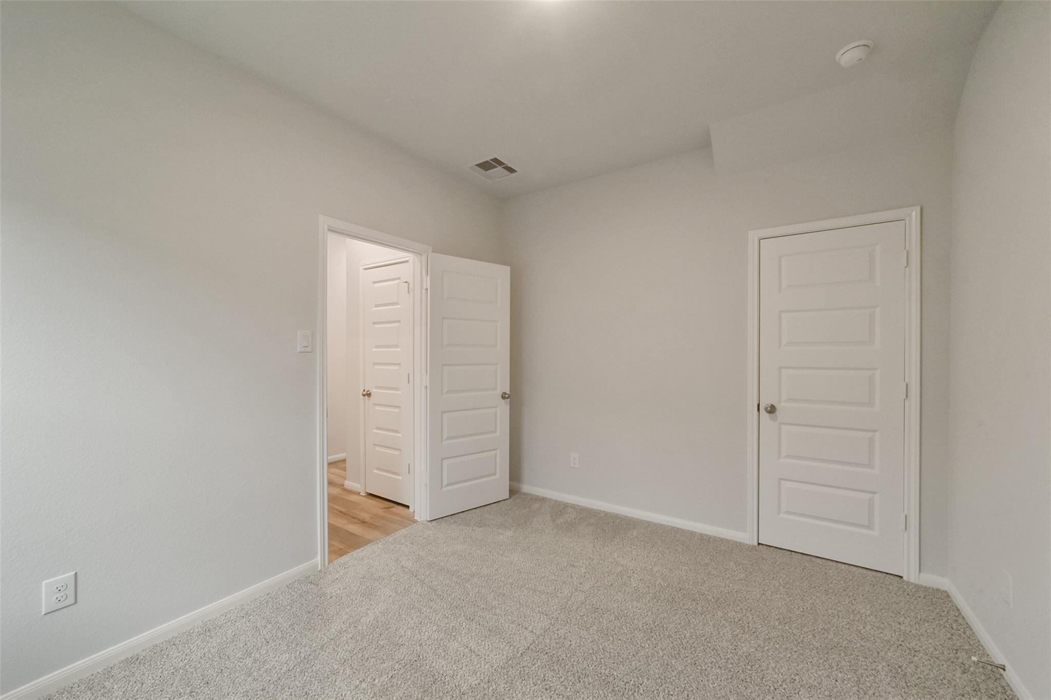 Light gray secondary bedroom with open white doors to adjoining room and neutral carpet in The San Marcos E 5-bedroom home, Beasley, Texas