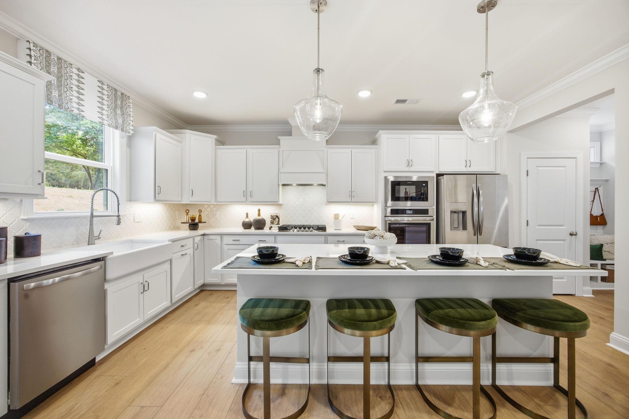 Spacious white kitchen at Enclave at Belmont in Belmont NC with central island, green velvet stools, farmhouse sink, and stainless appliances