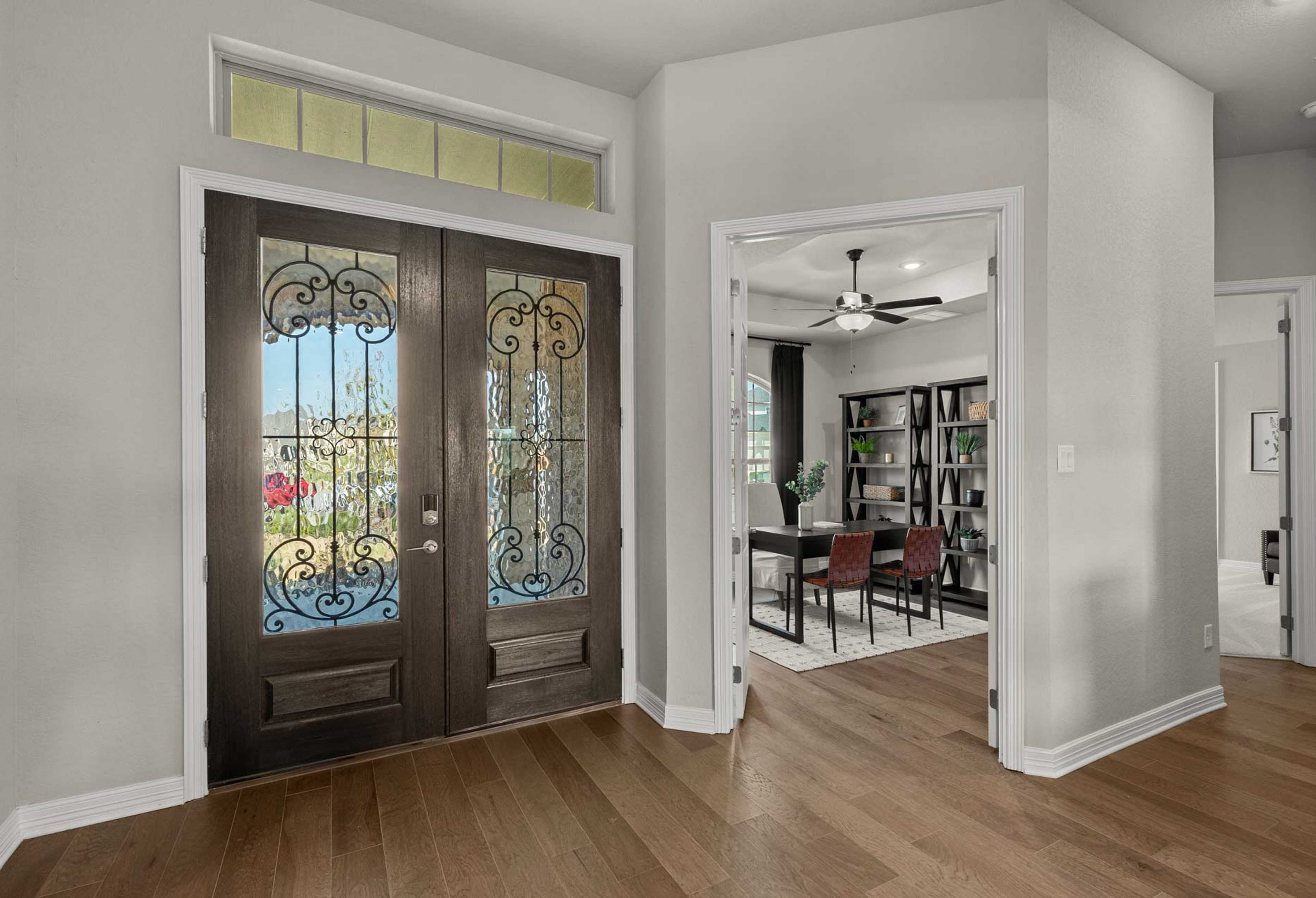 Elegant entryway of The Summerlin A with ornate wrought iron double doors, transom window, and adjacent study featuring bookshelves and dining table
