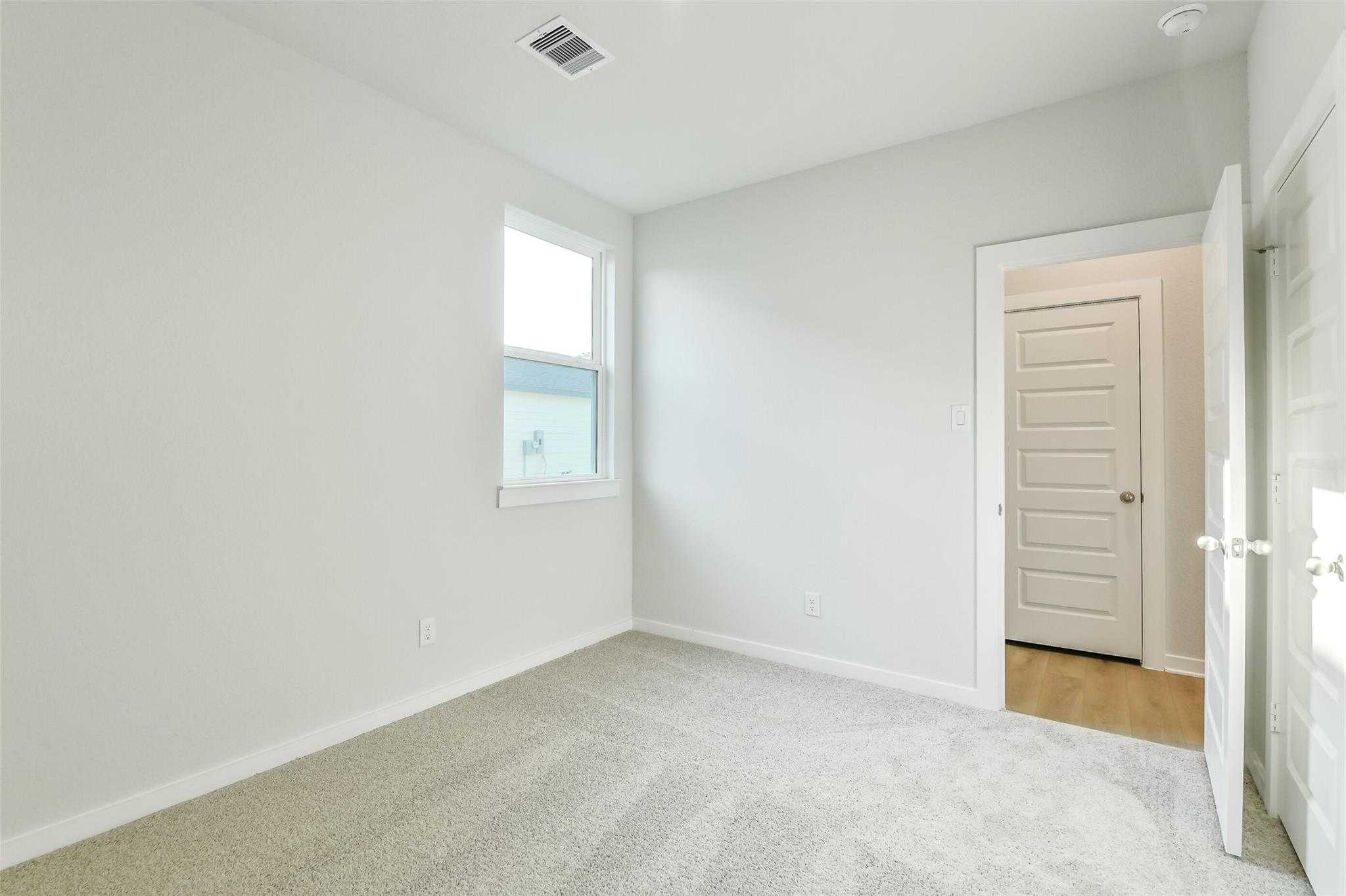 Bright secondary bedroom with light gray walls, beige carpet, window, and open door in Davidson Homes The Colorado F, Cleveland, Texas