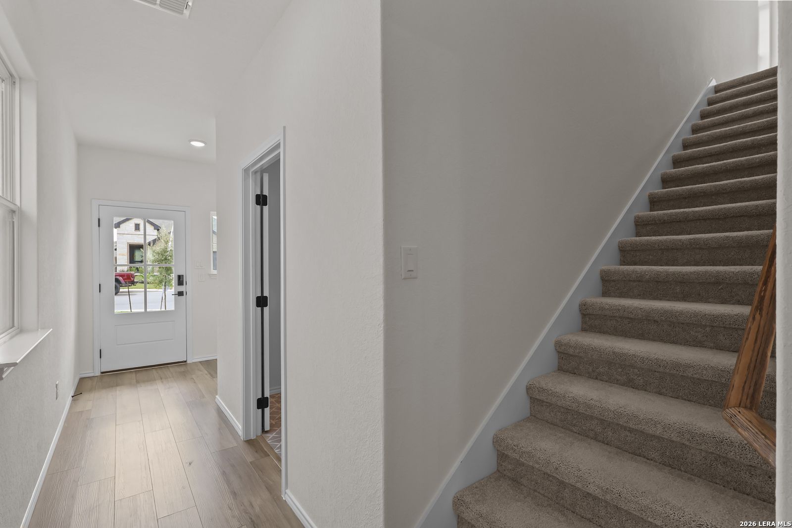 Bright foyer with glass-panel front door, wood-look tile flooring, and carpeted staircase in The Summit B, Morgan Meadows, San Antonio