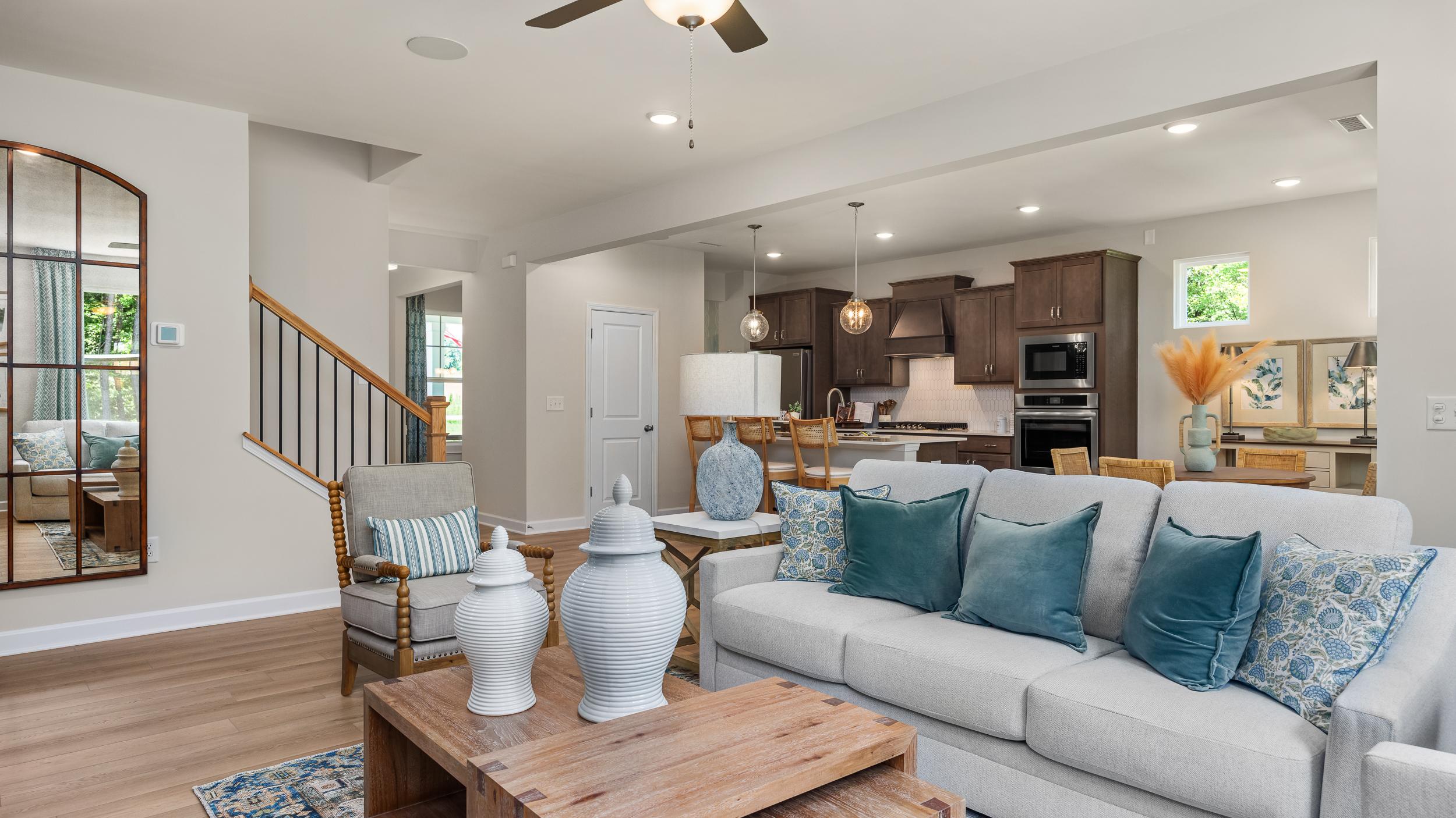 Open-concept living room at Retreat at North Main in Lillington NC with gray sectional sofa, hardwood floors, arched mirror, and modern kitchen