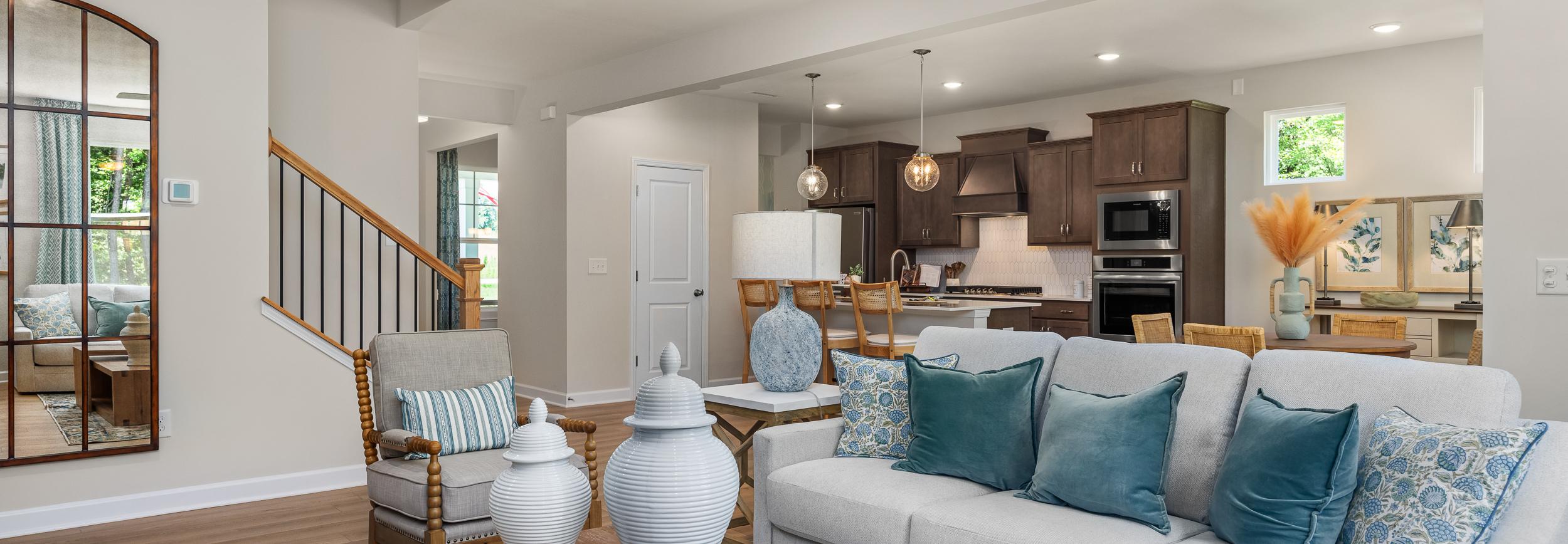Open-concept living room at Retreat at North Main in Lillington NC with gray sectional sofa, hardwood floors, arched mirror, and modern kitchen