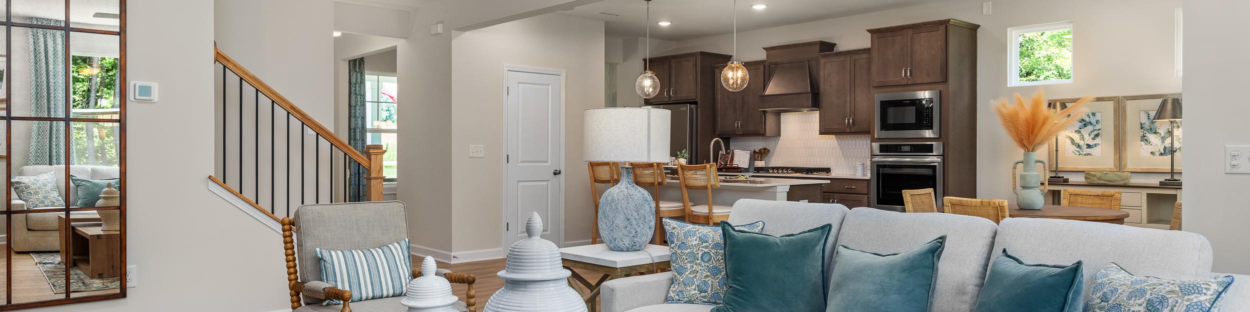 Open-concept living room at Retreat at North Main in Lillington NC with gray sectional sofa, hardwood floors, arched mirror, and modern kitchen