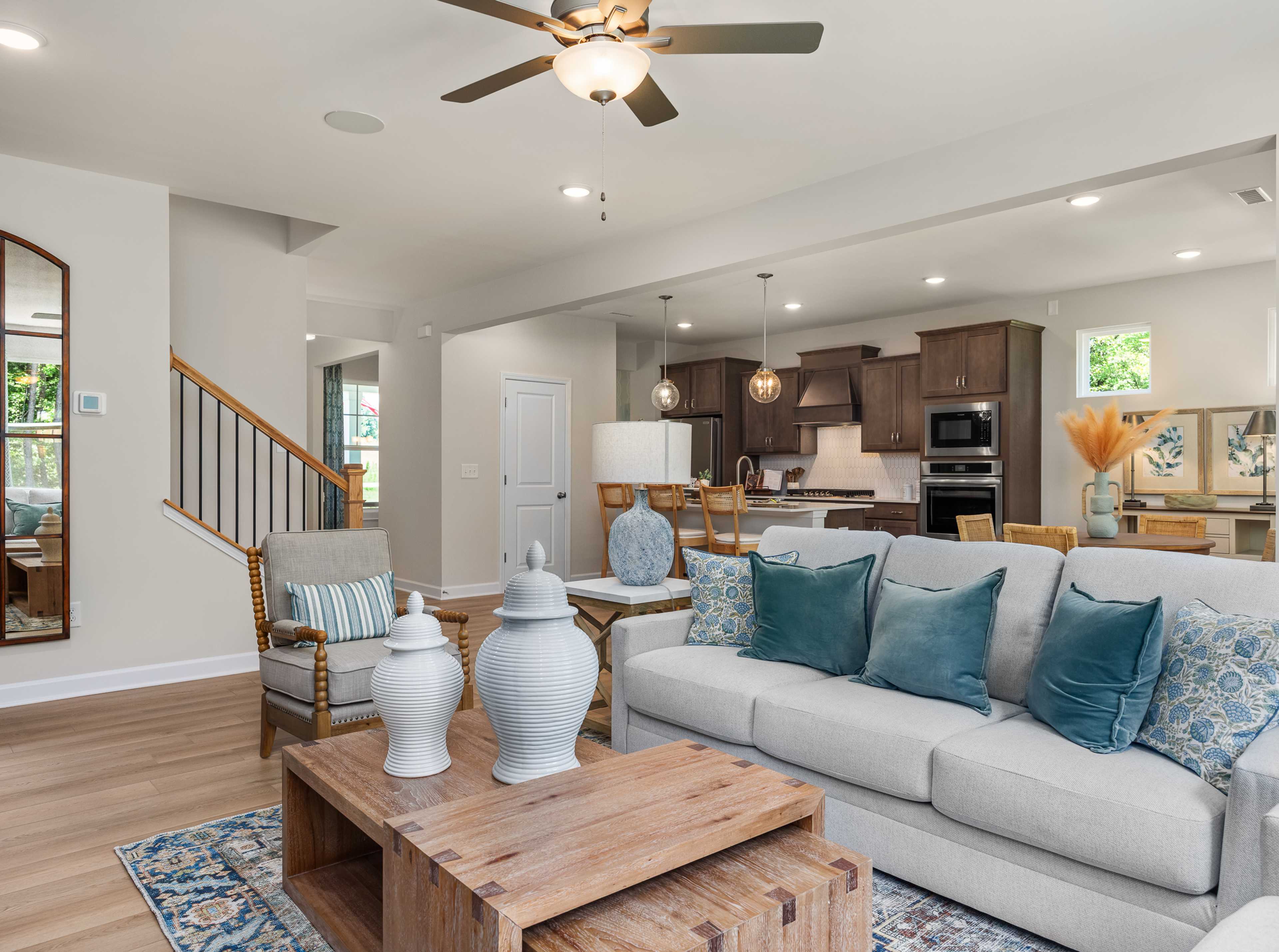 Open-concept living room at Retreat at North Main in Lillington NC with gray sectional sofa, hardwood floors, arched mirror, and modern kitchen