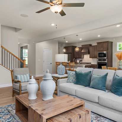 Open-concept living room at Retreat at North Main in Lillington NC with gray sectional sofa, hardwood floors, arched mirror, and modern kitchen