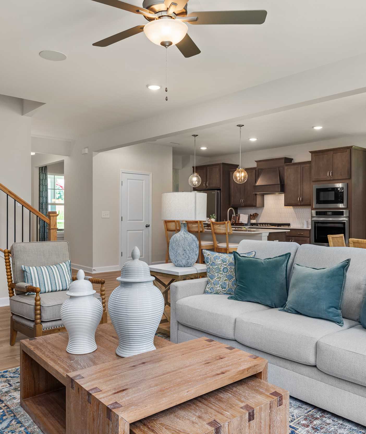 Open-concept living room at Retreat at North Main in Lillington NC with gray sectional sofa, hardwood floors, arched mirror, and modern kitchen