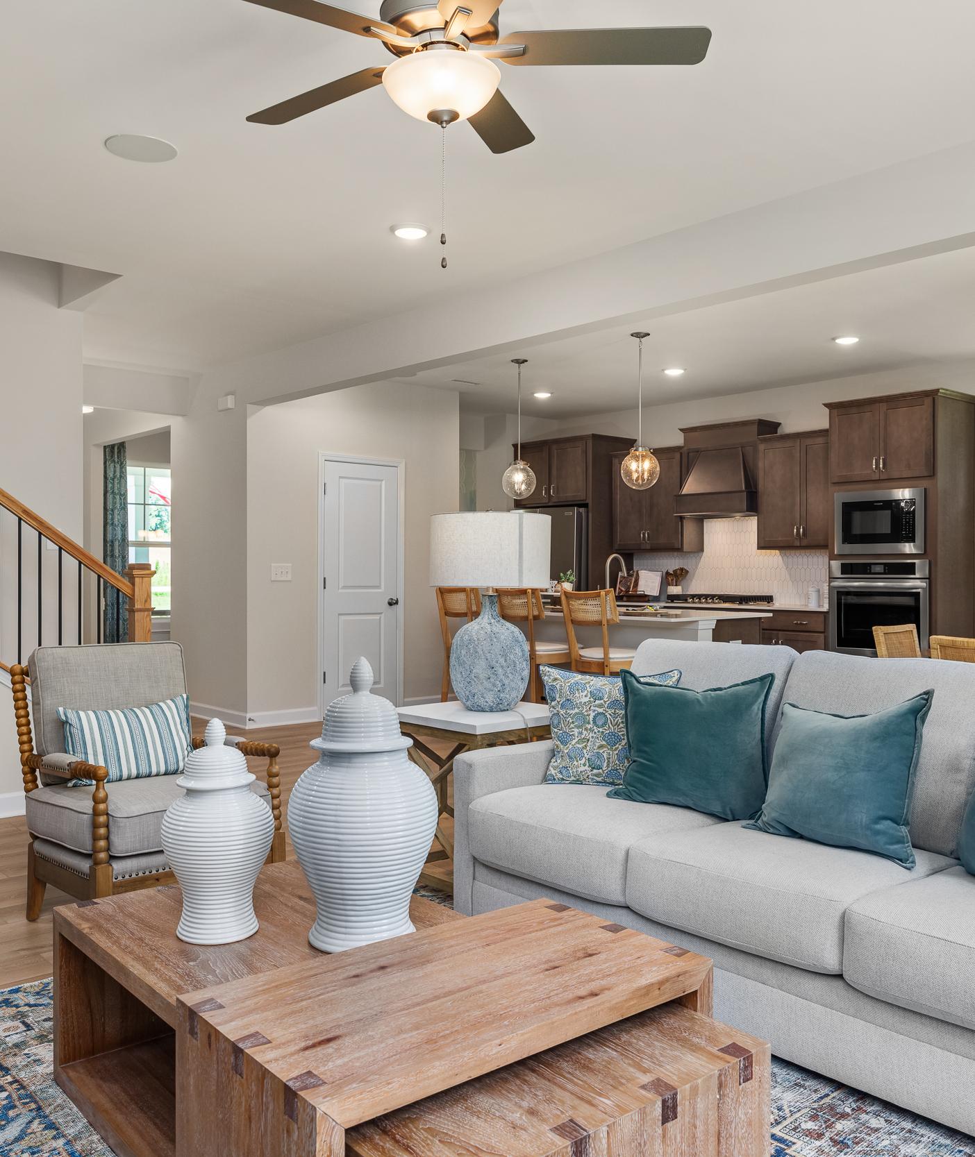 Open-concept living room at Retreat at North Main in Lillington NC with gray sectional sofa, hardwood floors, arched mirror, and modern kitchen