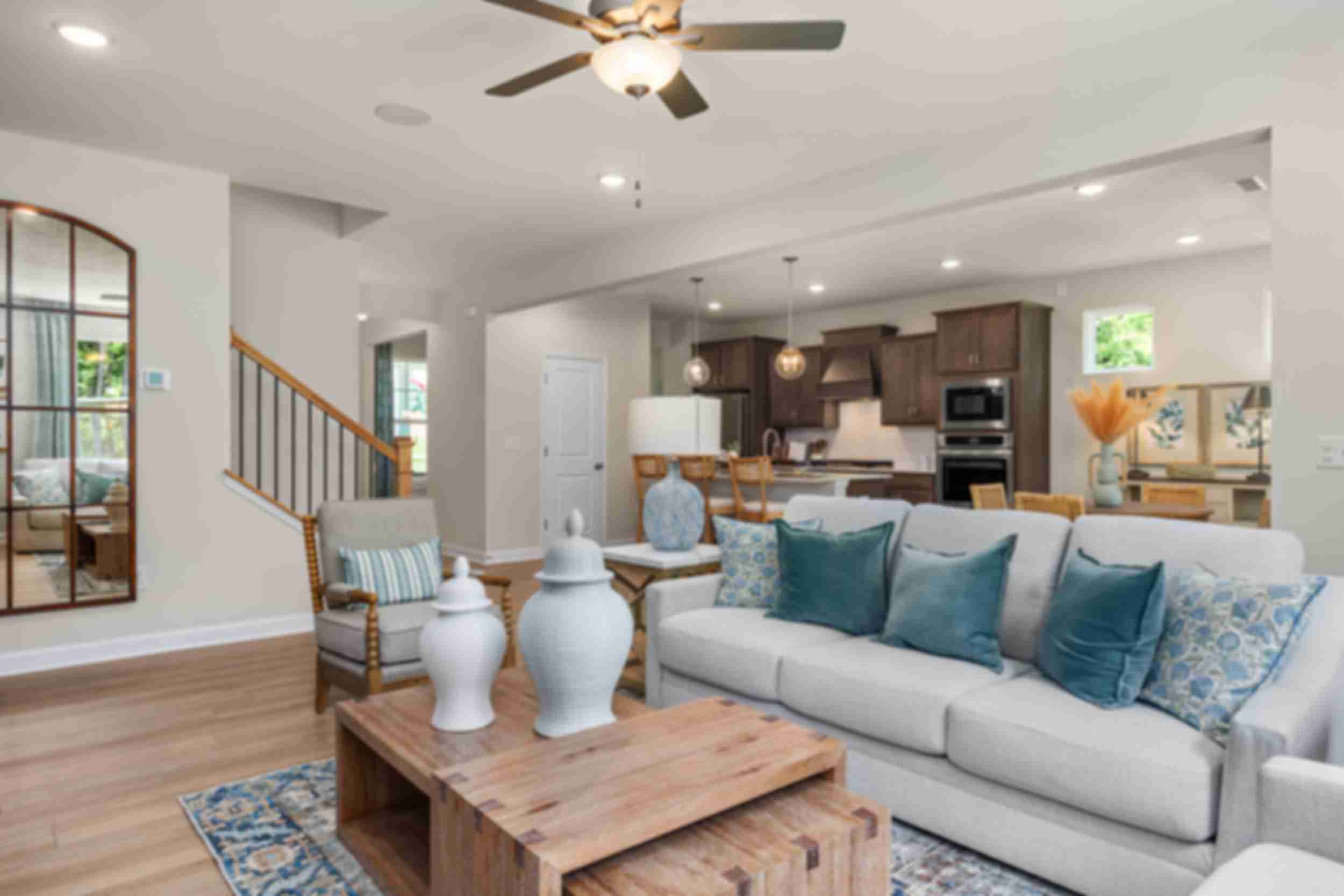 Open-concept living room at Retreat at North Main in Lillington NC with gray sectional sofa, hardwood floors, arched mirror, and modern kitchen