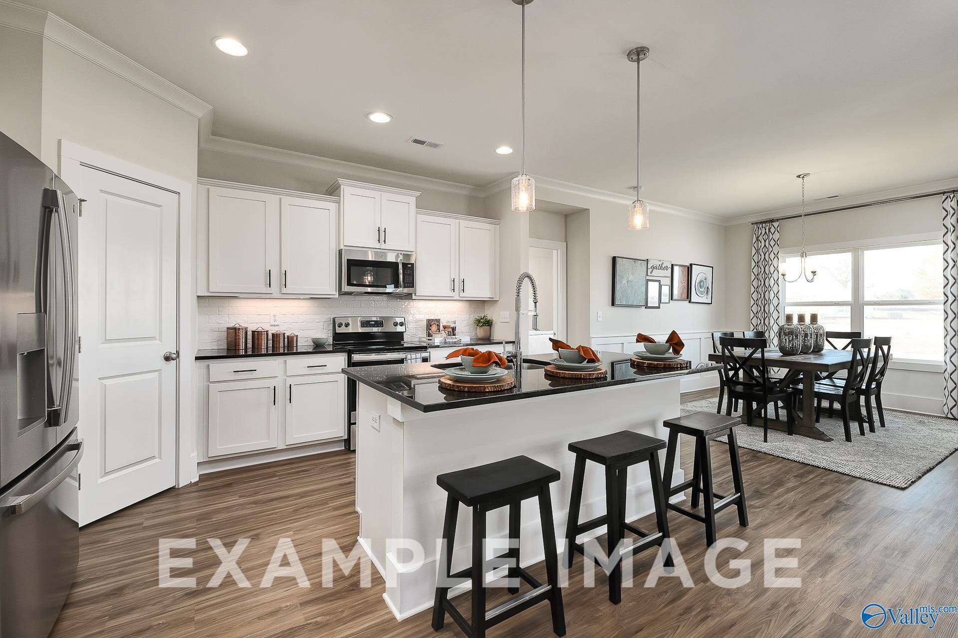 Open-concept kitchen with white cabinets and granite island in The Everett B floor plan at The Meadows, Athens, Alabama.