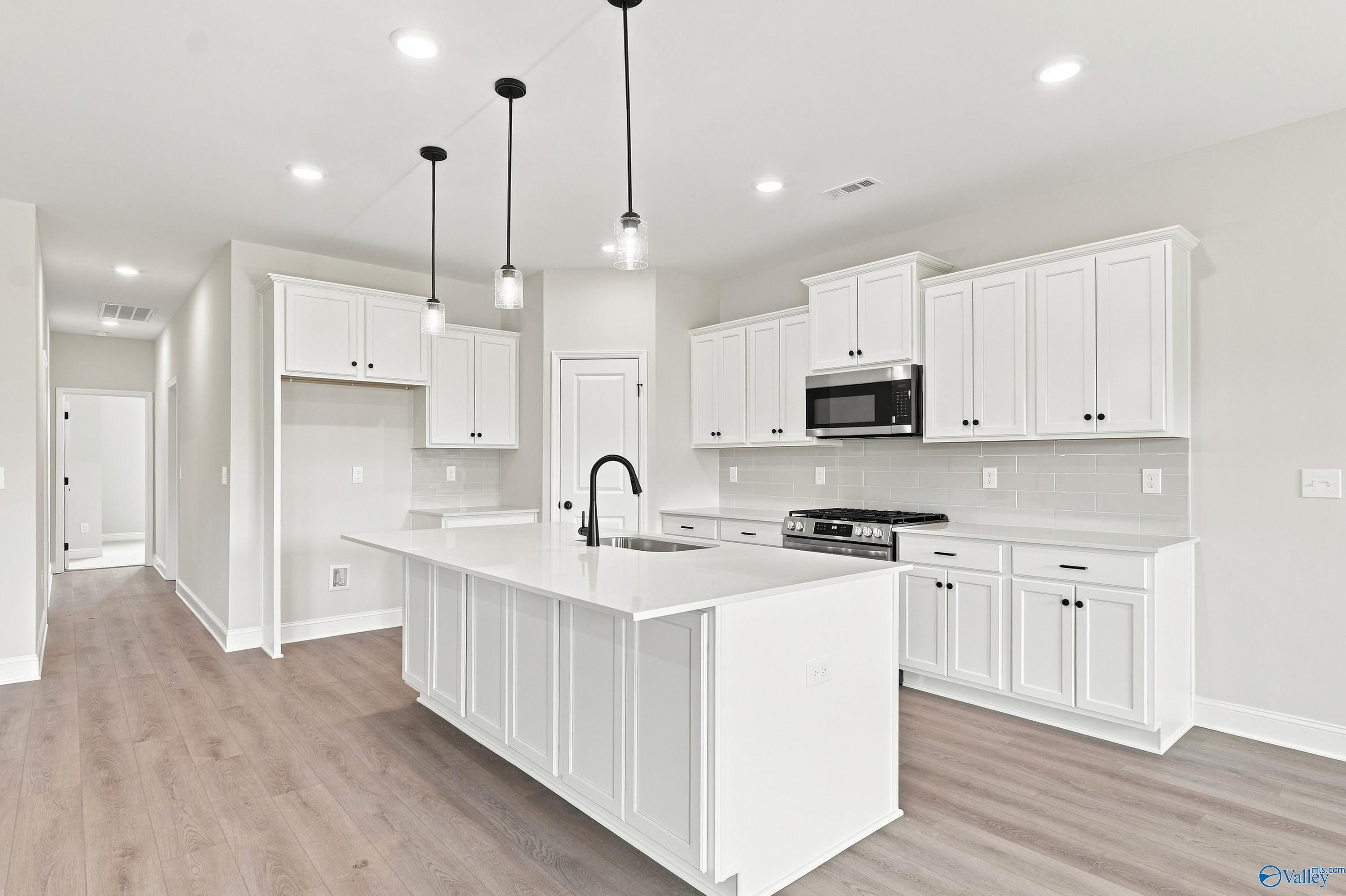 Modern kitchen with white cabinets, quartz island, and pendant lighting in The Rockford B plan at Kendall Downs, Toney, AL.