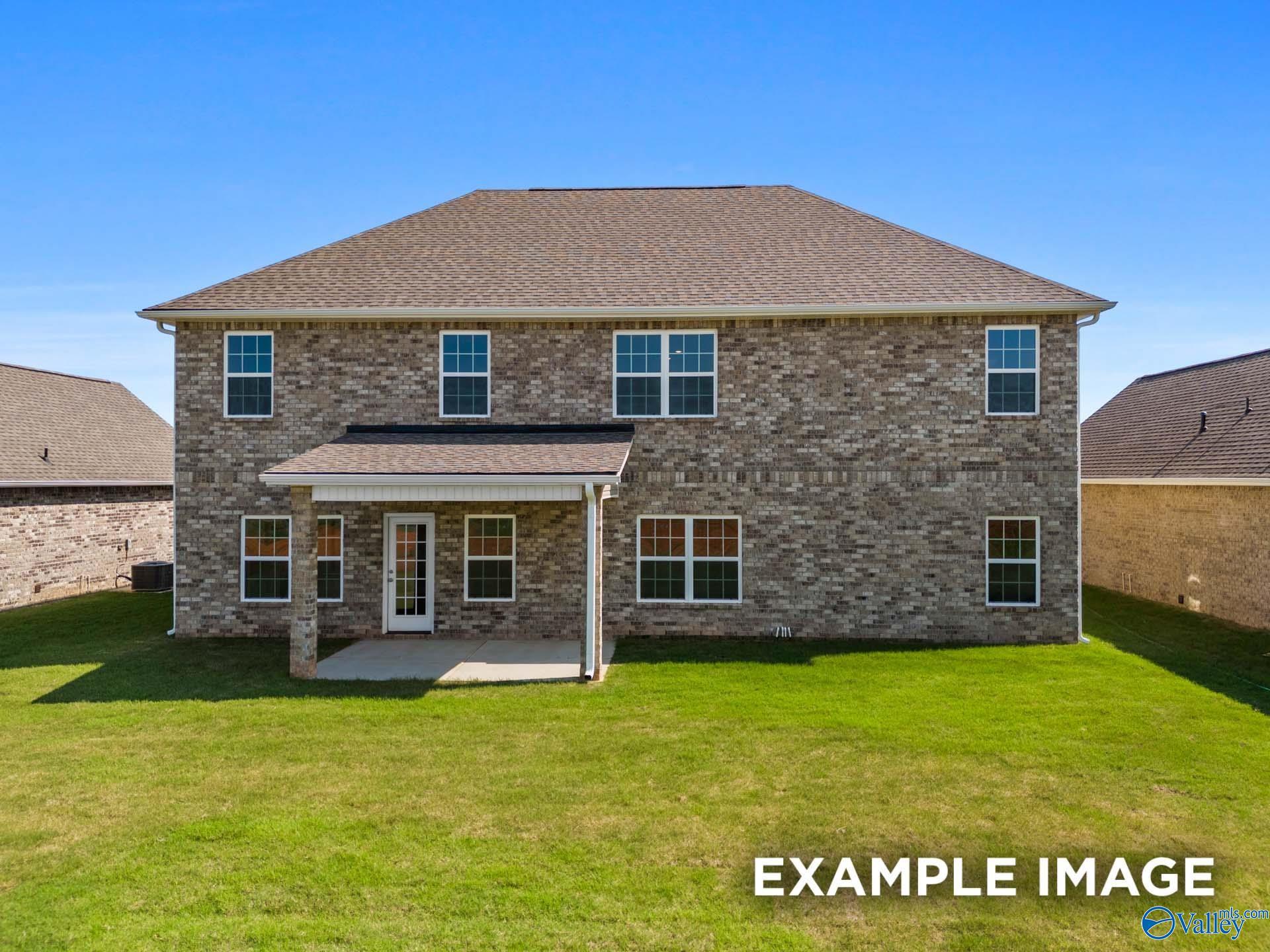 Covered back patio with brick exterior, glass door, and lush green lawn on 5-bedroom Madison A home in Toney, Alabama