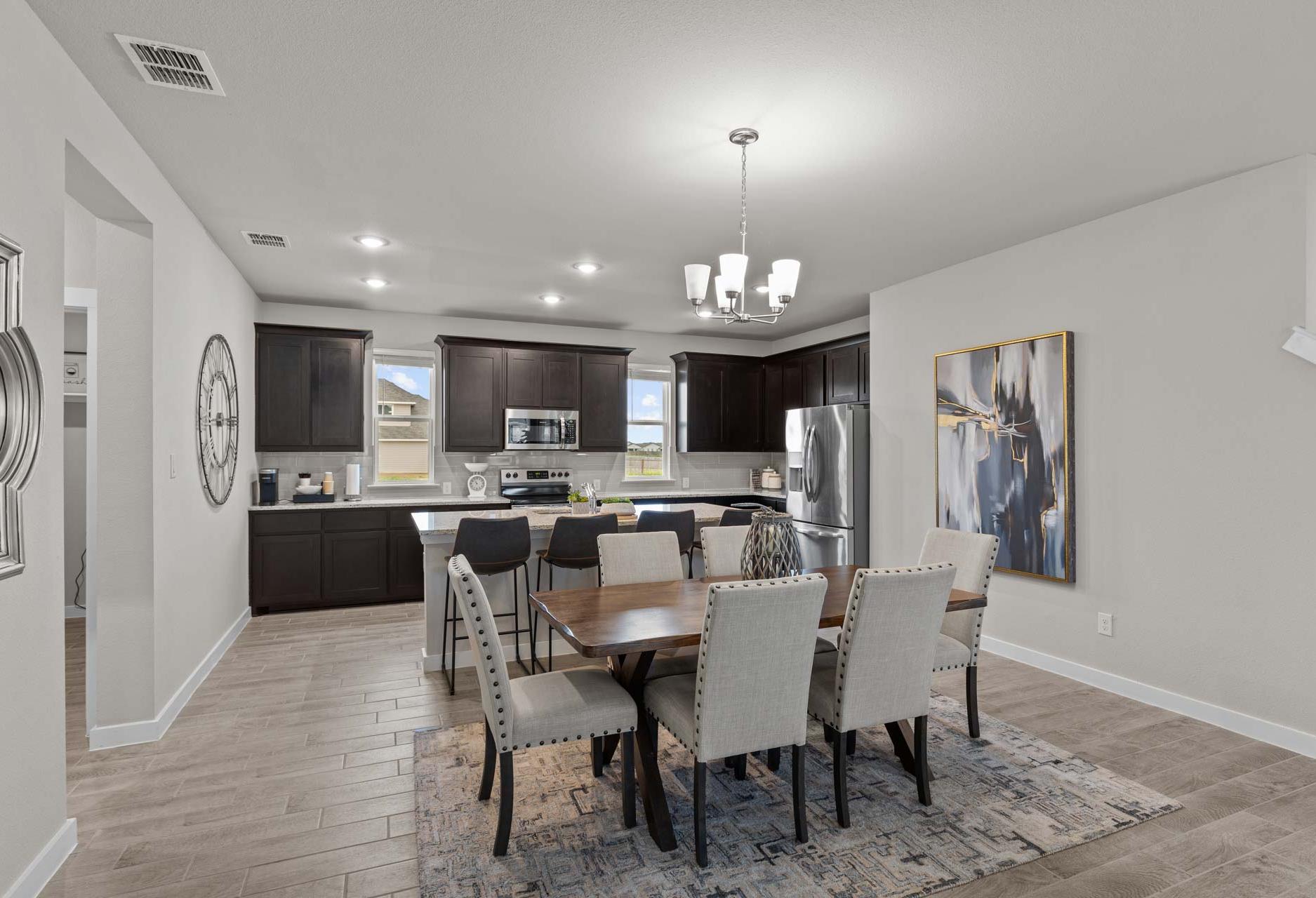 Spacious open-concept kitchen and dining in The Collin A home with dark cabinets, stainless appliances, large island, and chandelier
