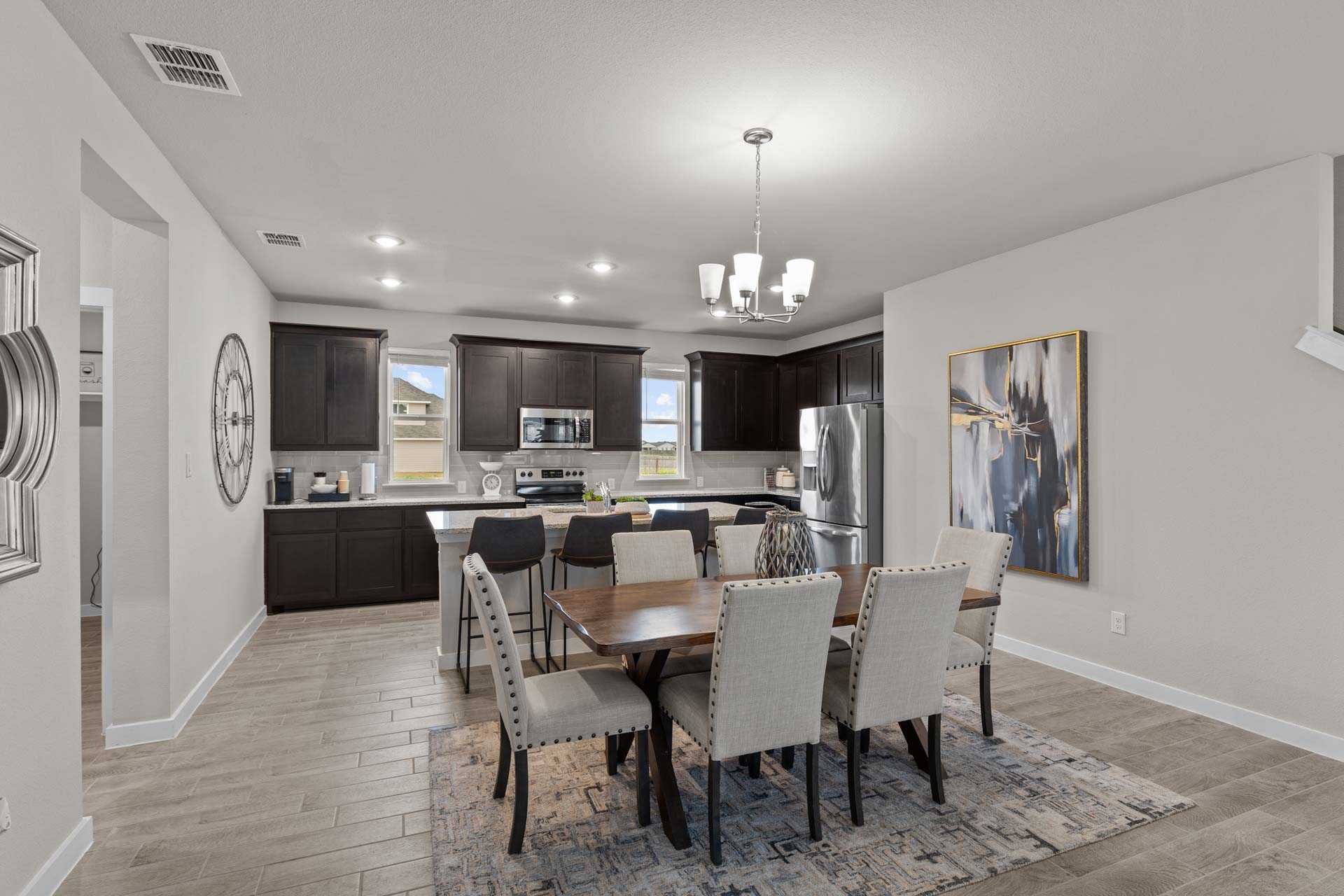 Spacious open-concept kitchen and dining in The Collin B featuring dark cabinets, stainless appliances, large wood table, and abstract wall art