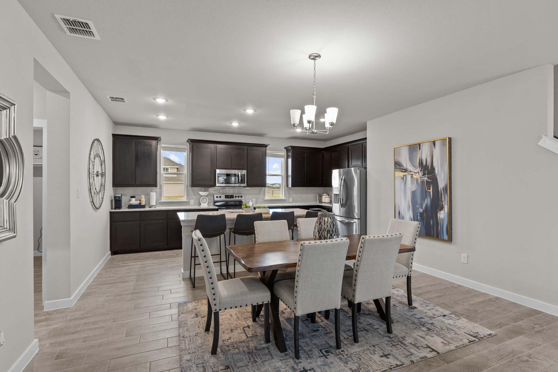 Spacious open-concept kitchen and dining in The Collin A home with dark cabinets, stainless appliances, large island, and chandelier