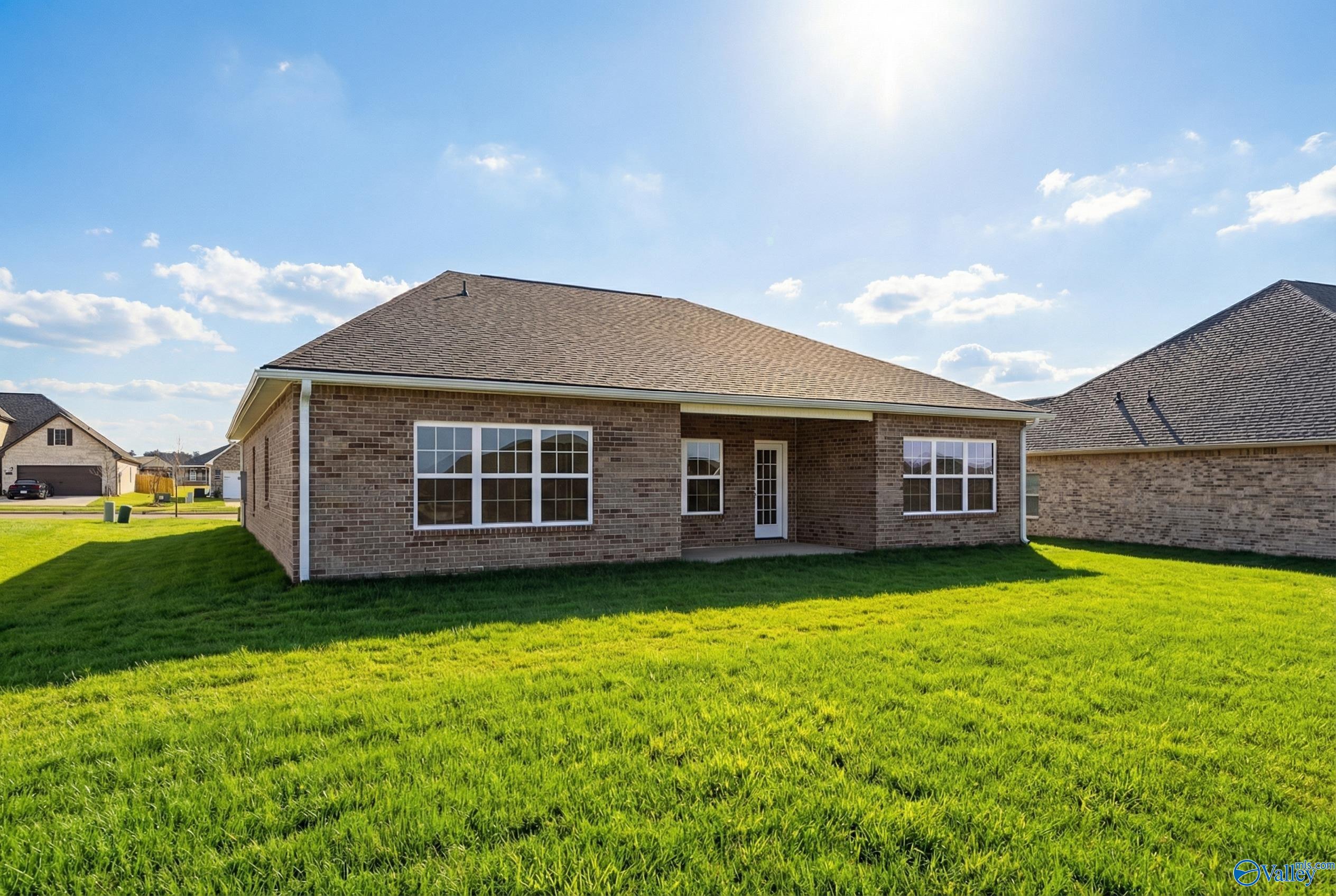 Single-story brick home with gabled roof, covered patio, large windows, and lush green lawn in Creekside, Harvest, Alabama