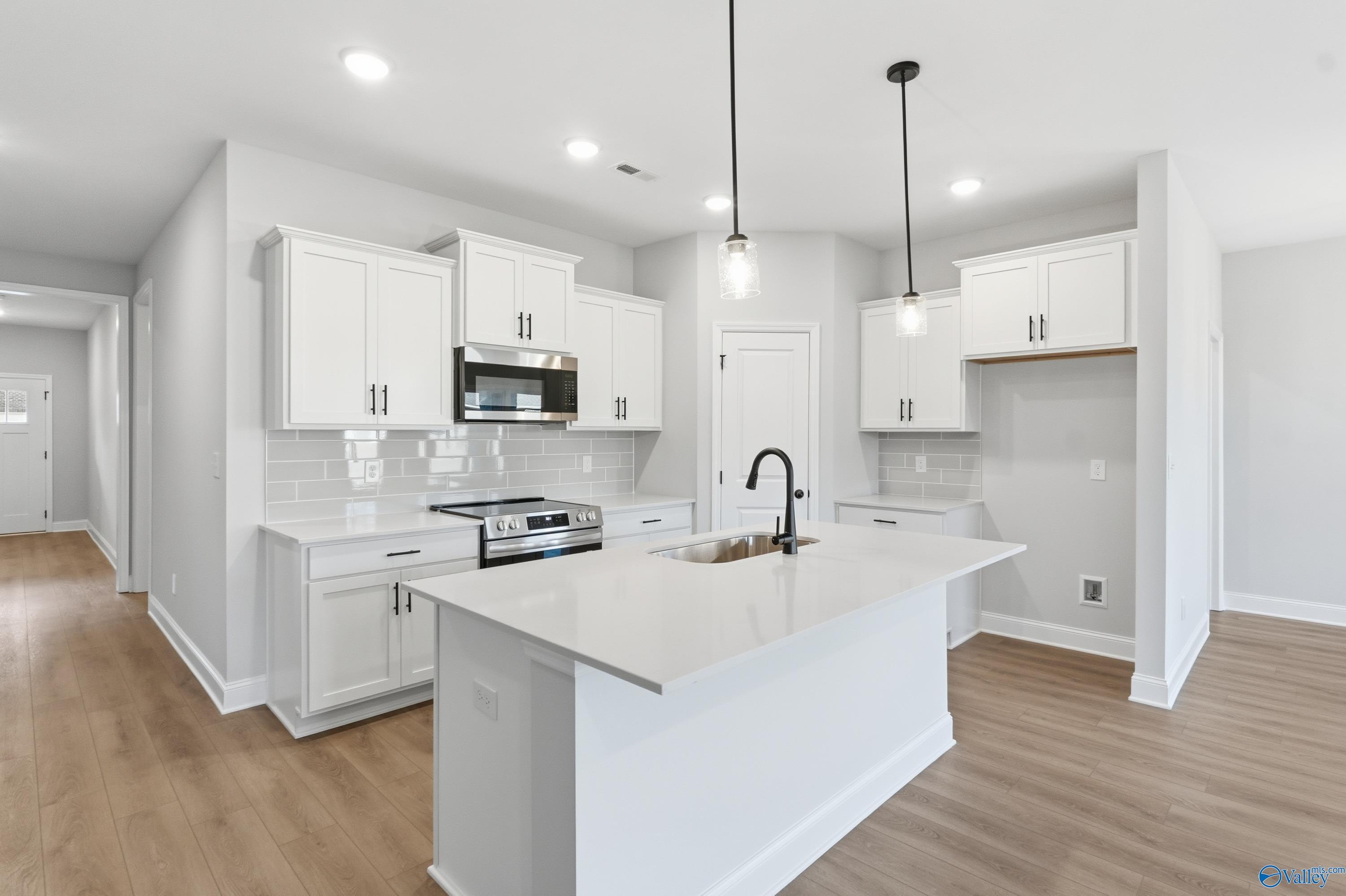 Bright white kitchen with large quartz island, stainless steel appliances, subway tile backsplash in Davidson Homes Daphne D, Arab AL
