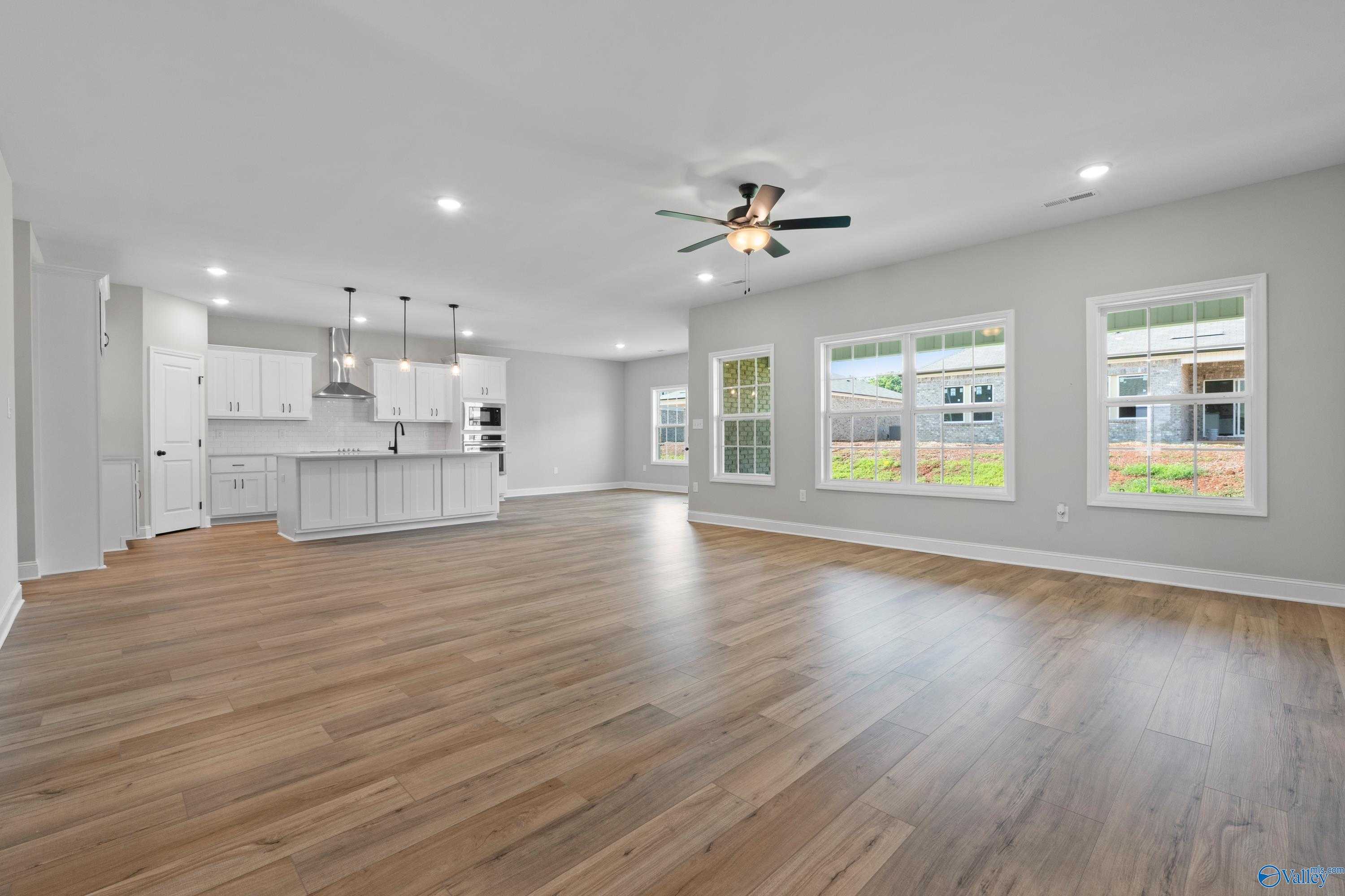 Spacious open-concept kitchen with white cabinets, large island, hardwood floors, and large windows in Davidson Homes The Rockford, Toney, Alabama