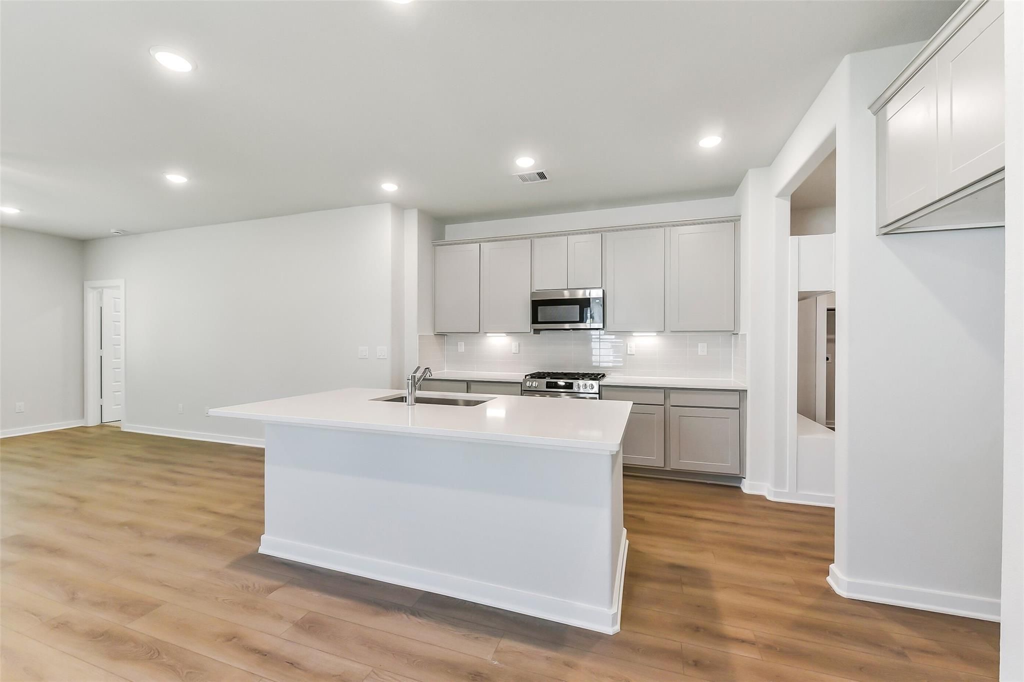 Spacious modern kitchen with white island, quartz counters, stainless appliances in 5-bed The Brazos E by Davidson Homes, Magnolia TX