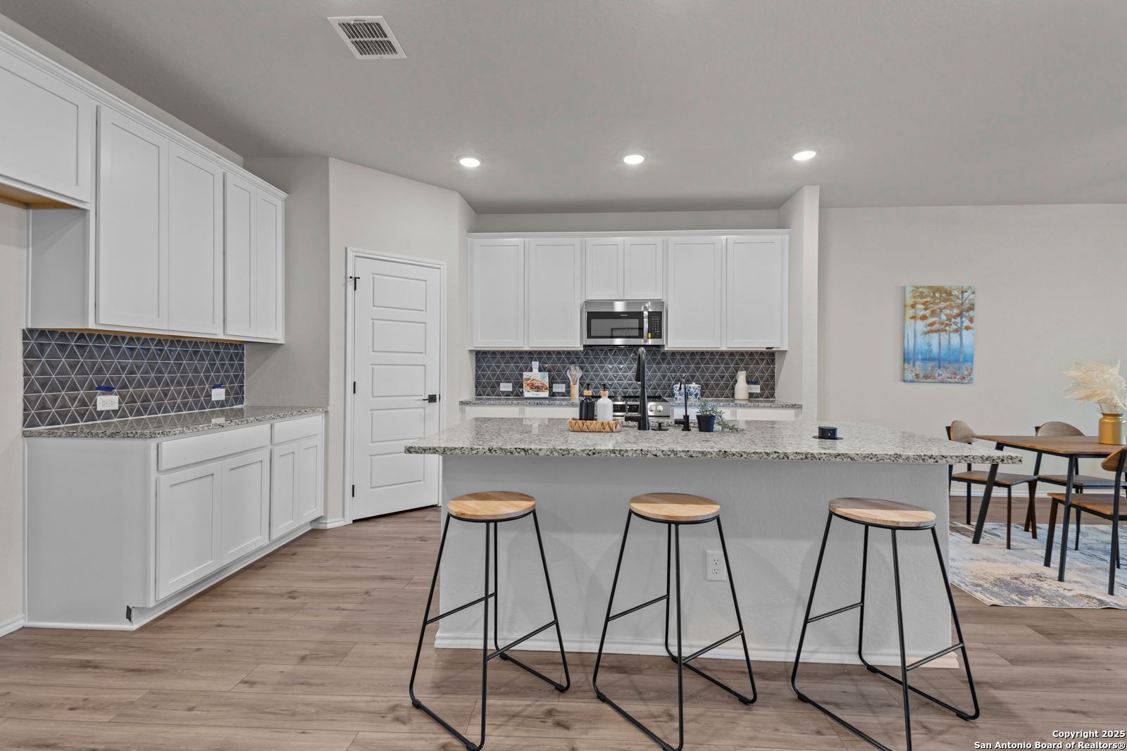 Modern kitchen with white cabinets, blue backsplash, stainless appliances, and island bar in Davidson Homes The Douglas C, Seguin, Texas