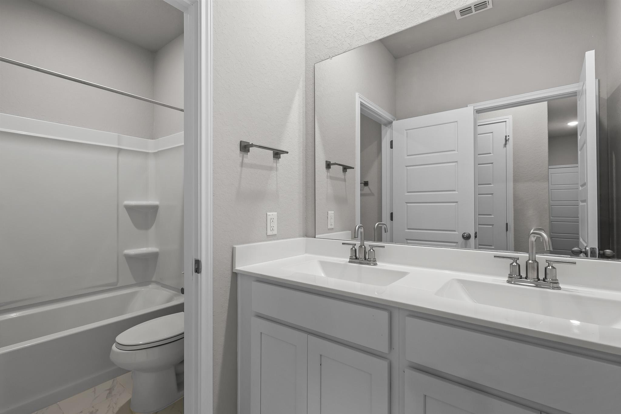 Modern bathroom in The Colorado B featuring a dual-sink vanity, large mirror, and a tub-shower combo.