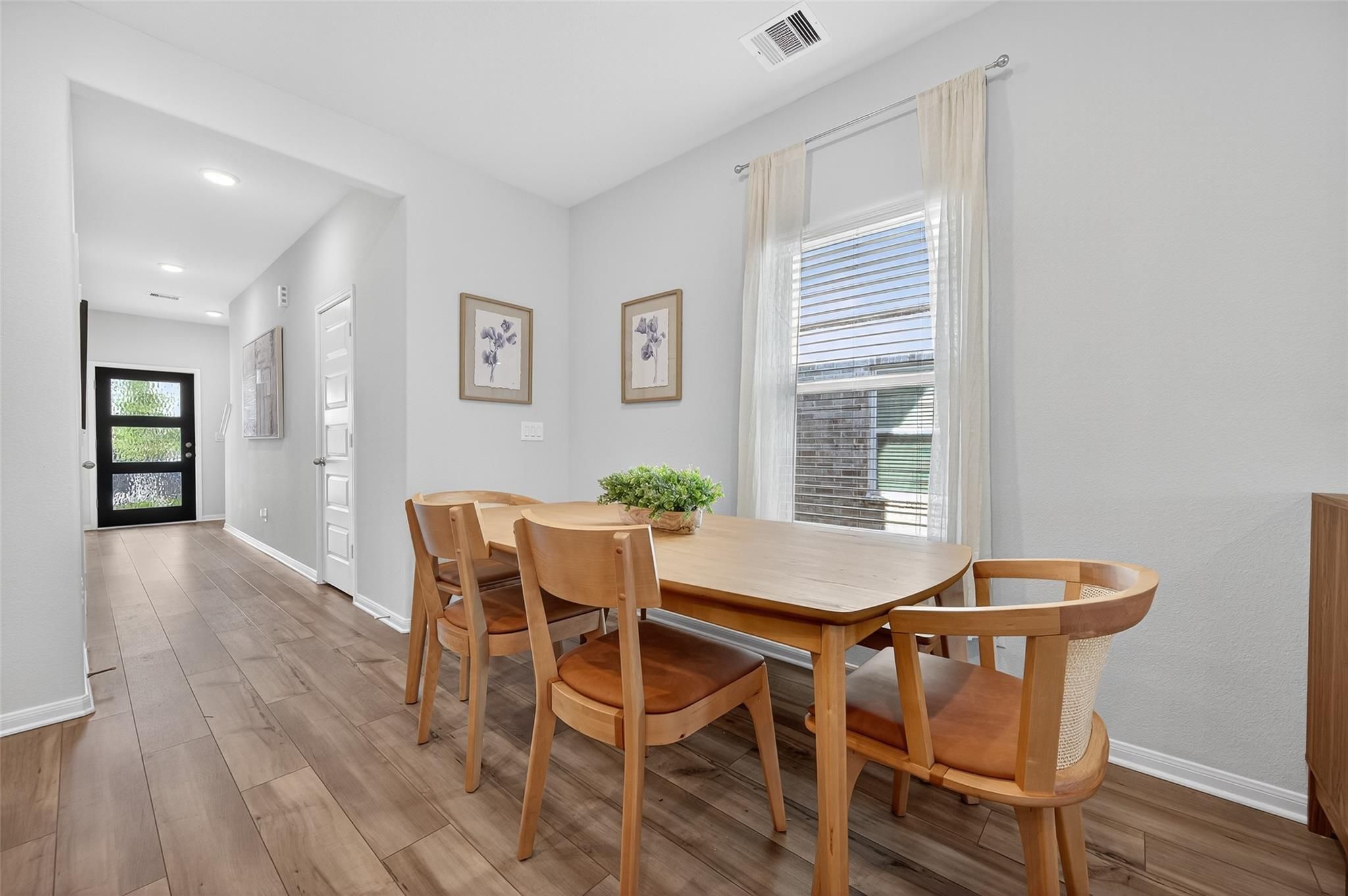 Modern dining room with oak table, leather chairs, and centerpiece plant in 5-bedroom Davidson Homes The Brazos E, Magnolia Texas