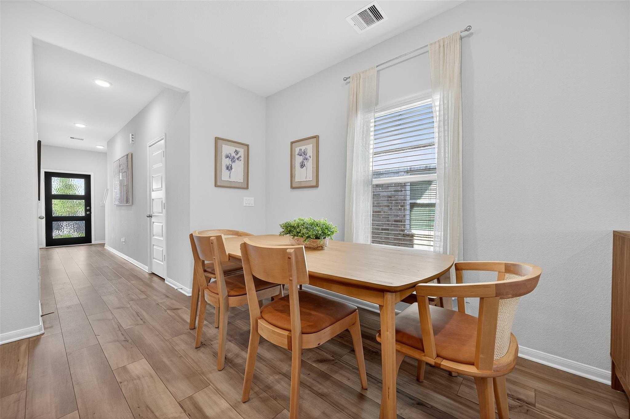 Modern dining room with oak table, leather chairs, and centerpiece plant in 5-bedroom Davidson Homes The Brazos E, Magnolia Texas